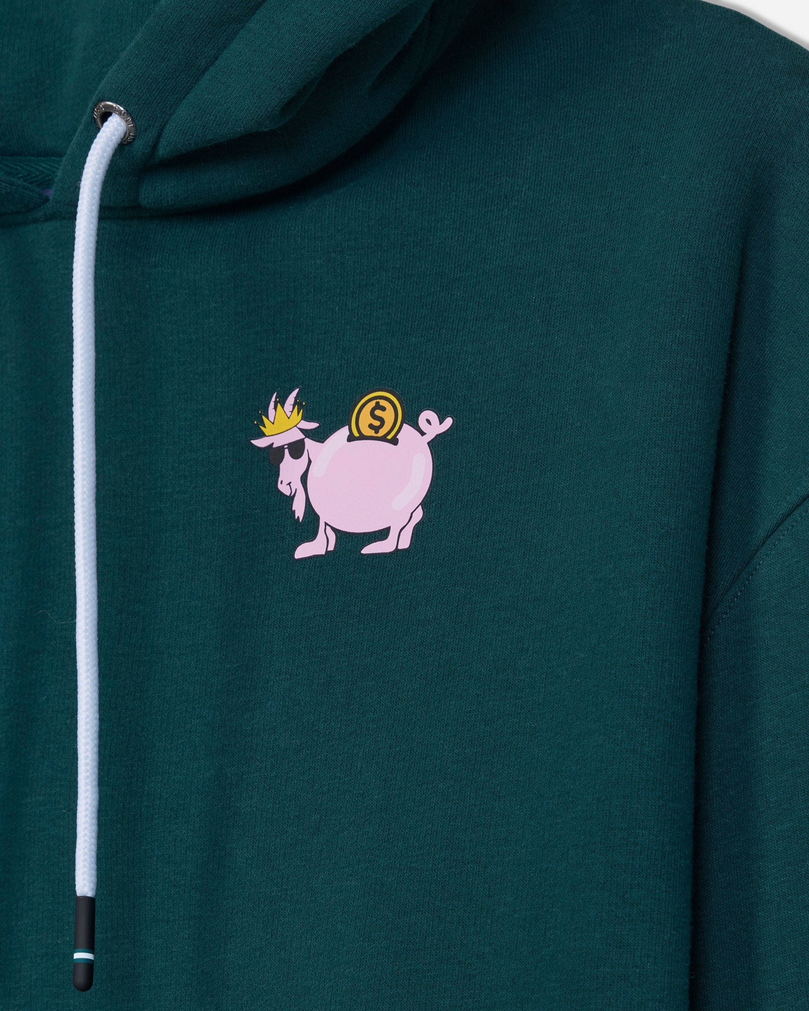 Close-up of a dark green hoodie featuring a small graphic of a pink goat carrying a gold coin on its back, with a white drawstring on the left side.