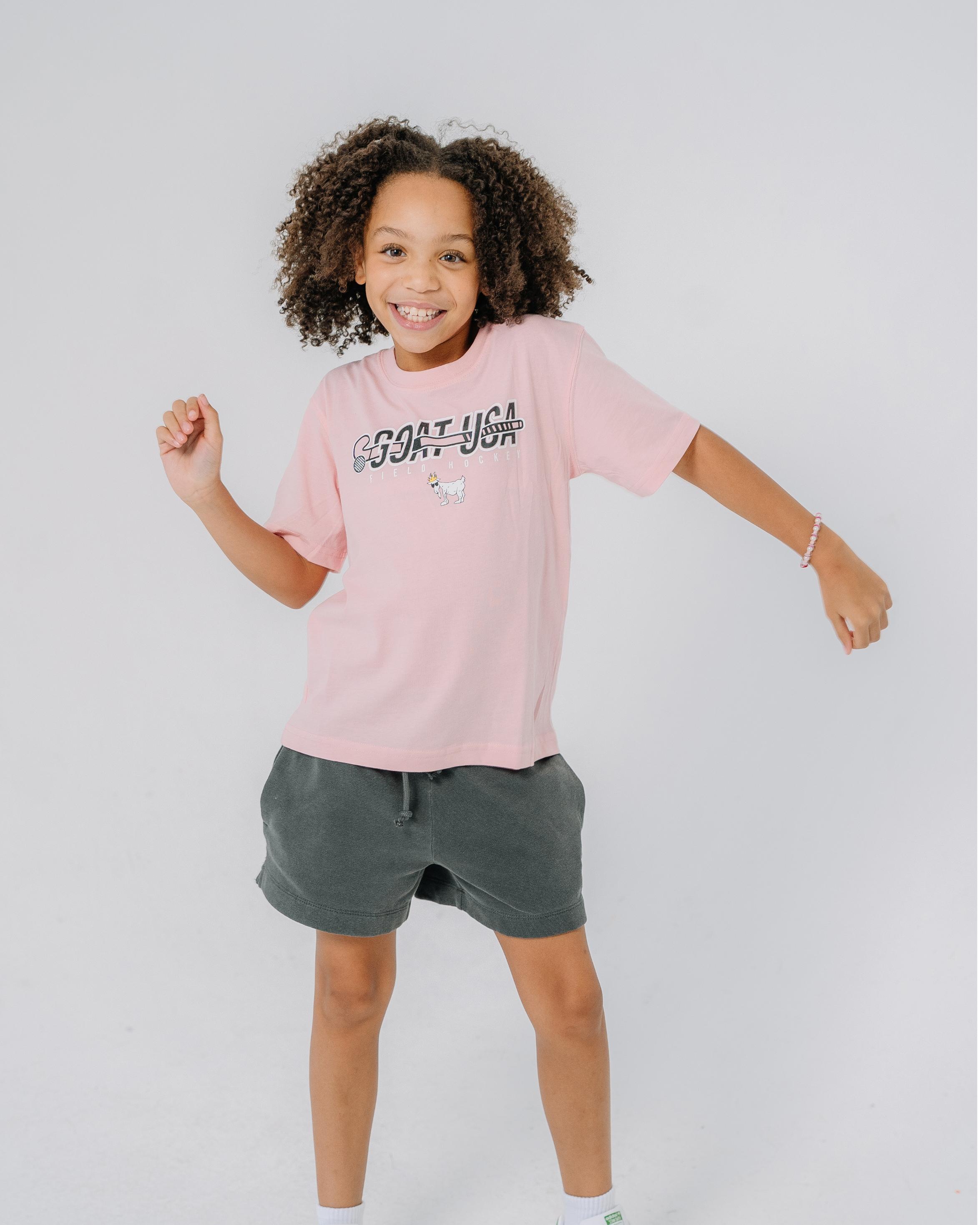Kid wearing pink shirt with field hockey stick that goes through the wording "GOAT USA"