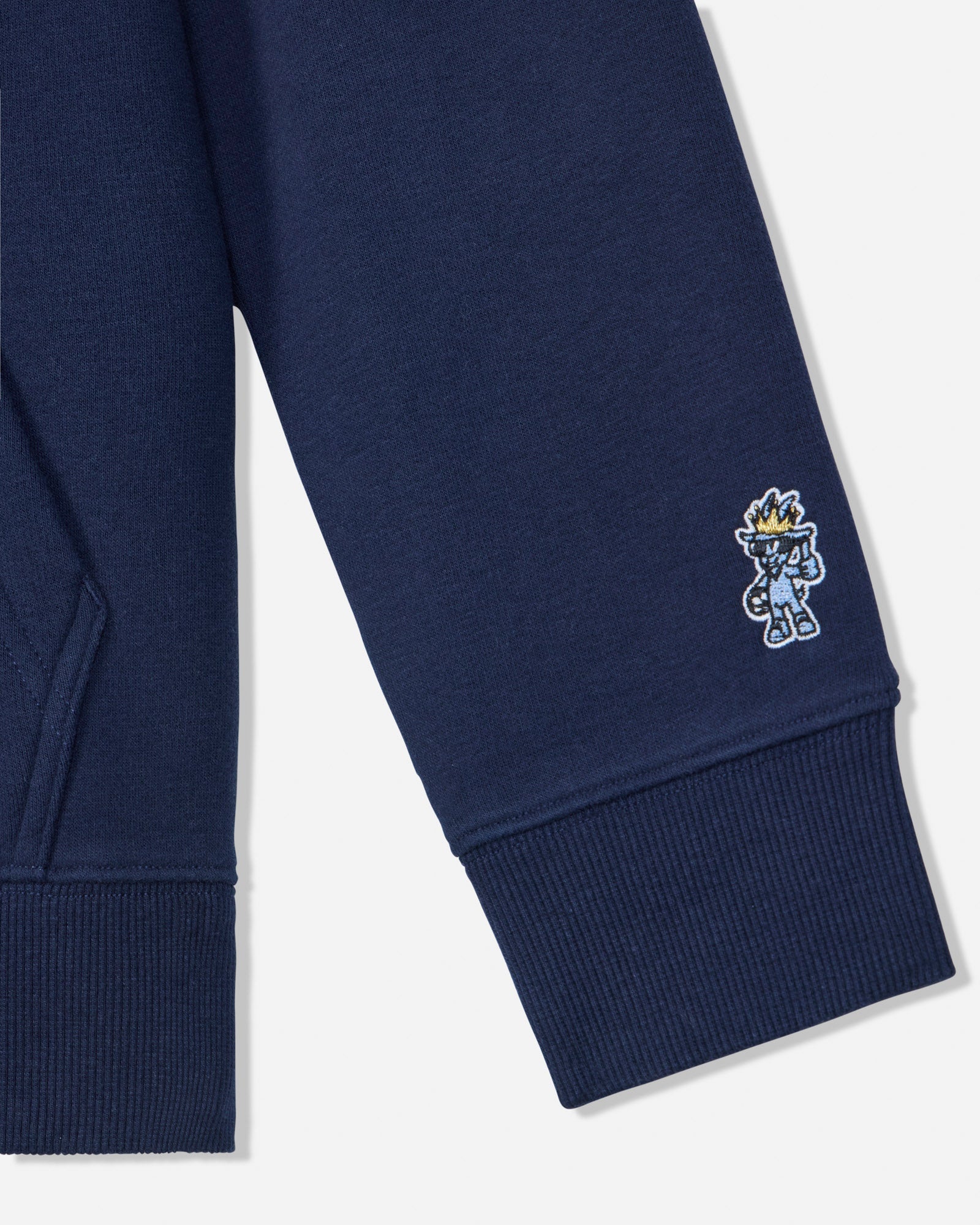 Close-up of a navy blue ribbed sweatshirt sleeve with a small embroidered cartoon character on the cuff, shown against a light gray background.