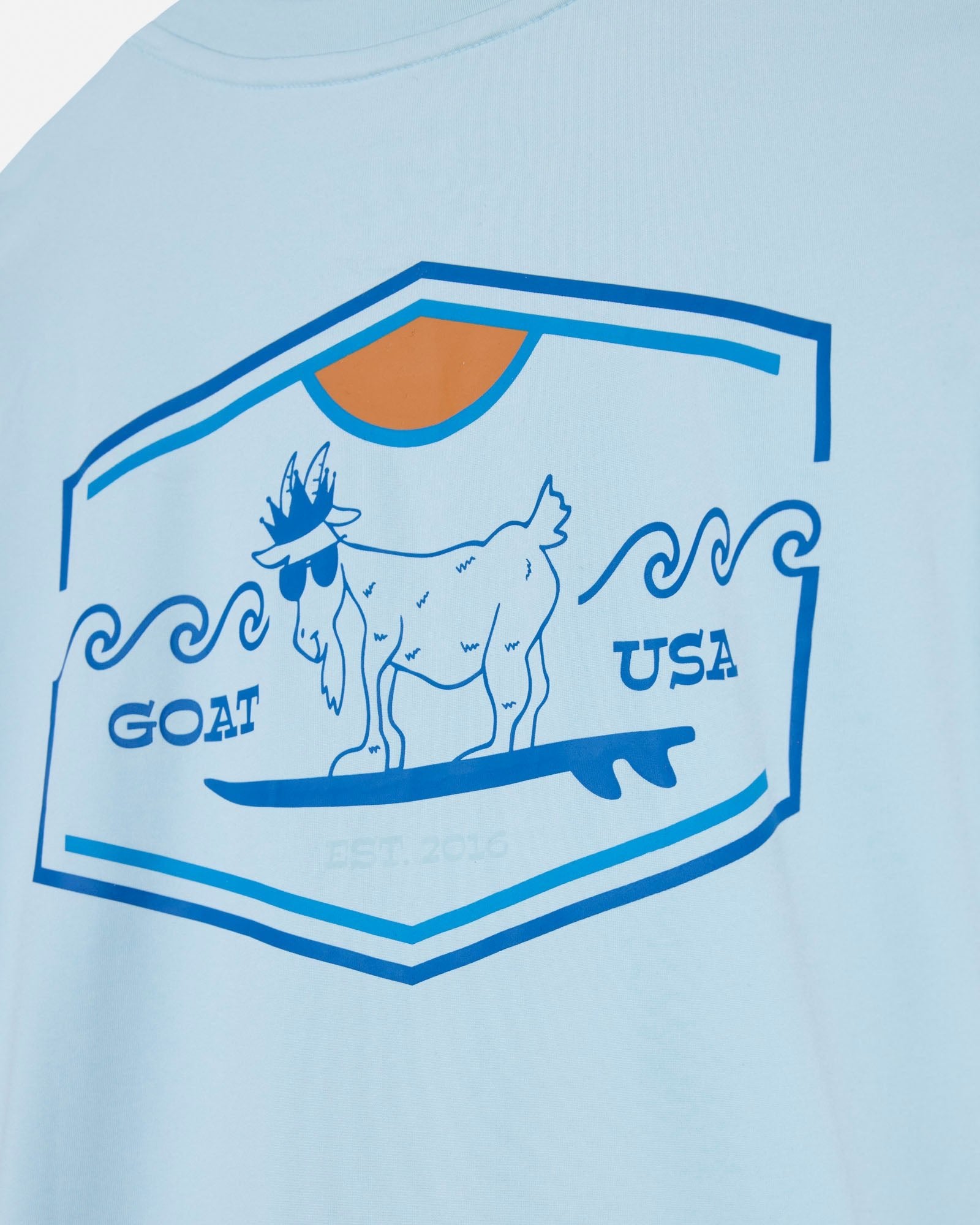 Light blue t-shirt with a graphic of a goat on a surfboard and 'GOAT USA' text, on a light blue background.#color_delicate-blue
