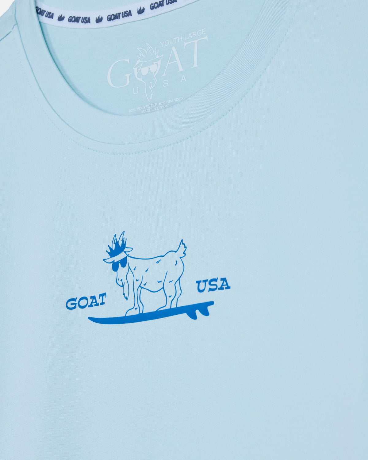 Light blue t-shirt with a graphic of a goat on a surfboard and 'GOAT USA' text.