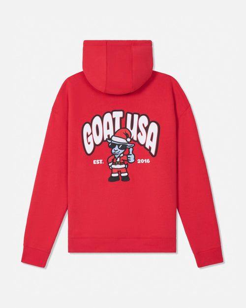 A red pullover hoodie shown from the back, featuring a large graphic print of the text 'GOAT USA' in white with black outlines and a cartoon goat character wearing a Santa hat and holding a gift. The text 'EST. 2016'