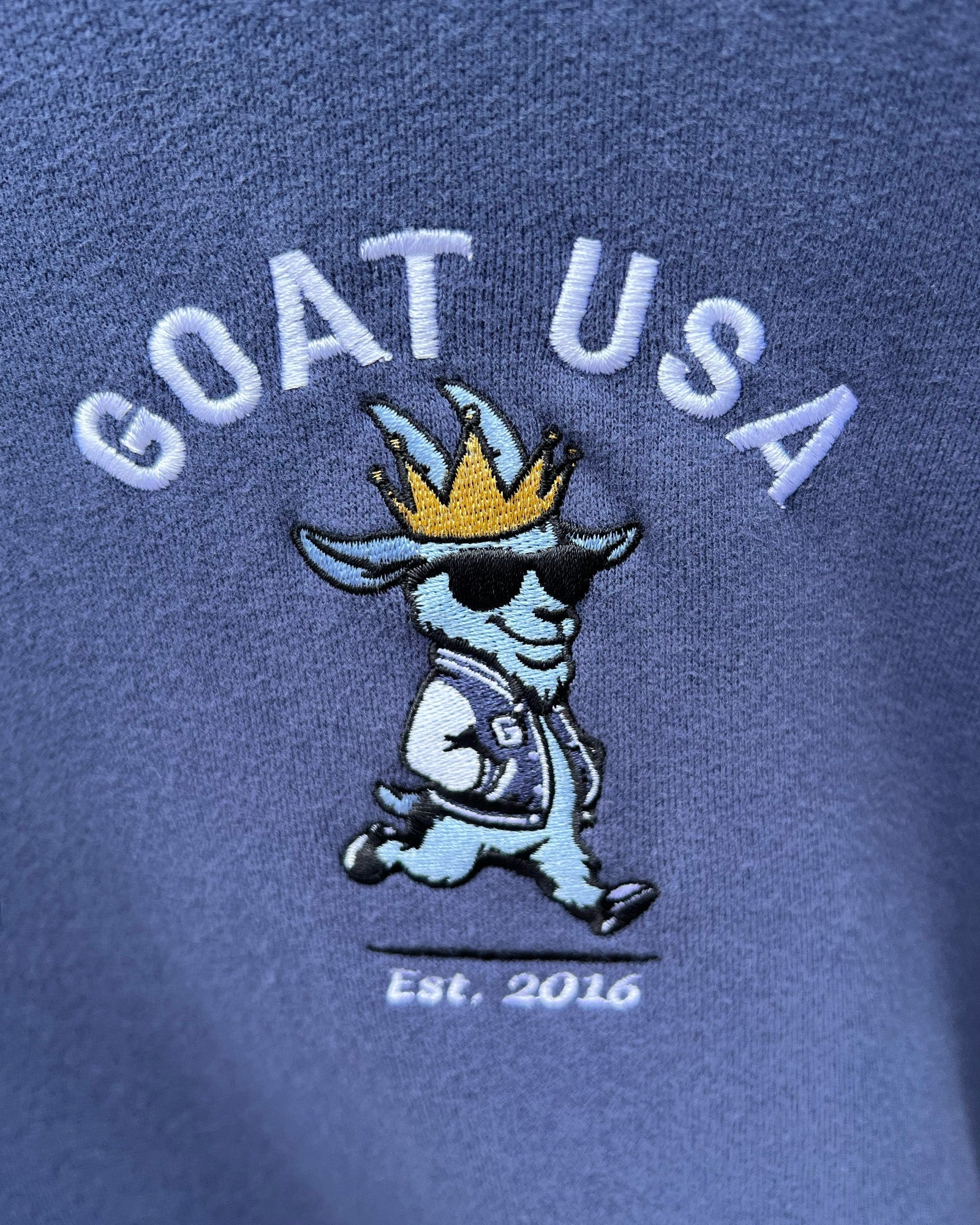 Embroidered design on blue fabric with 'GOAT USA' text and cartoon goat character.