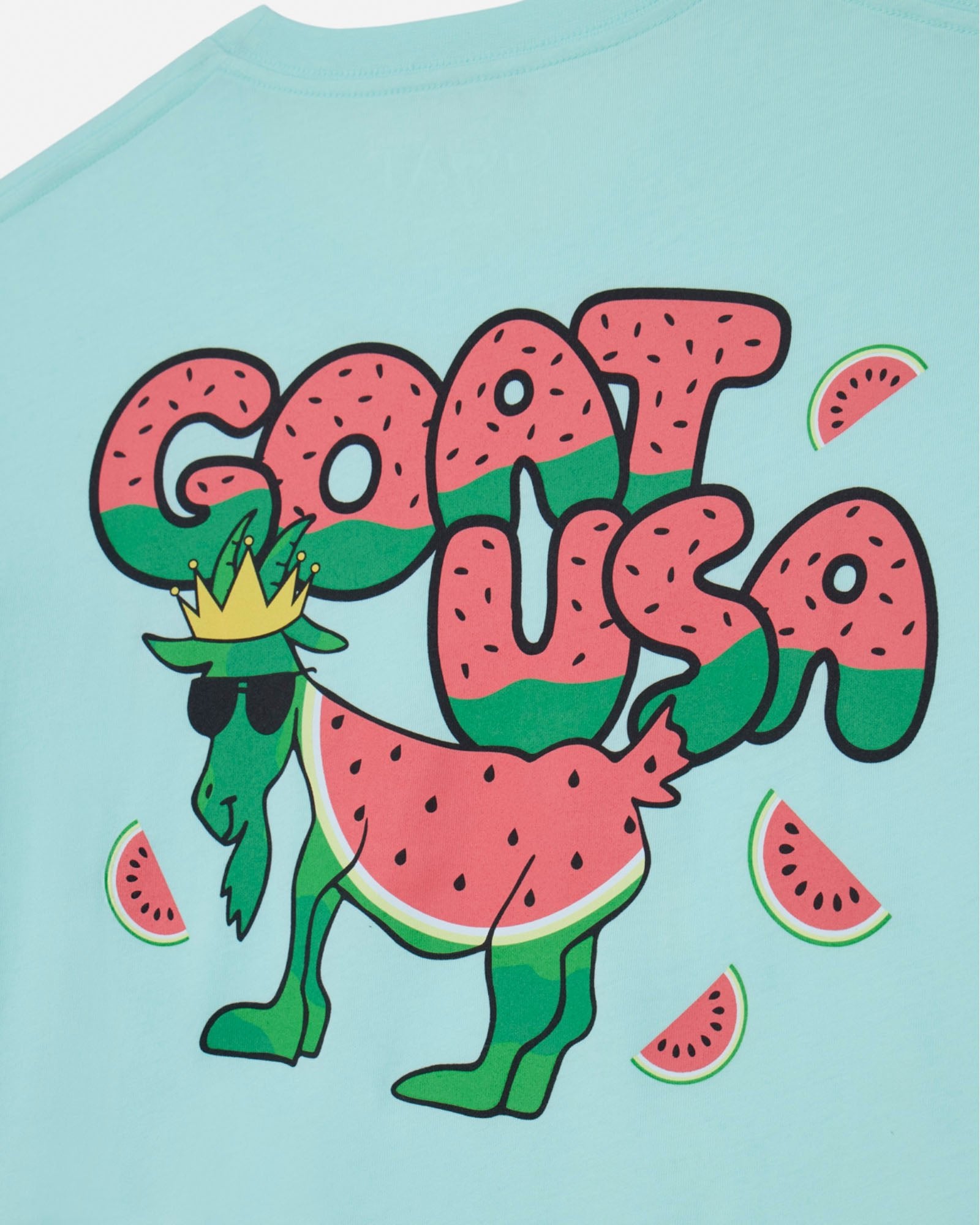 Light green t-shirt with a cartoon goat wearing sunglasses and a crown, surrounded by watermelon slices on a light gray background.