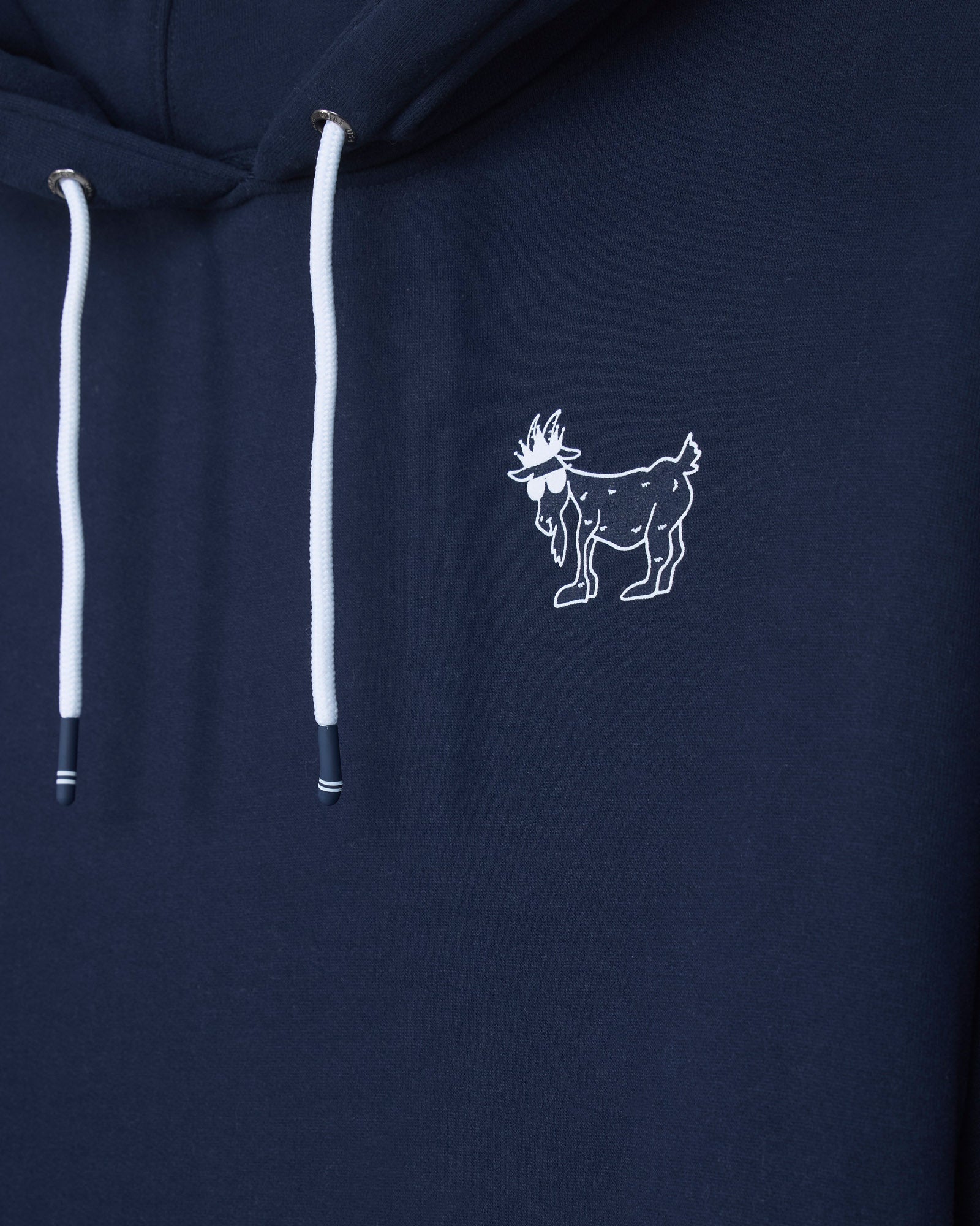 Close-up of a navy blue hoodie featuring white drawstrings and a small white embroidered goat logo on the chest.#color_navy