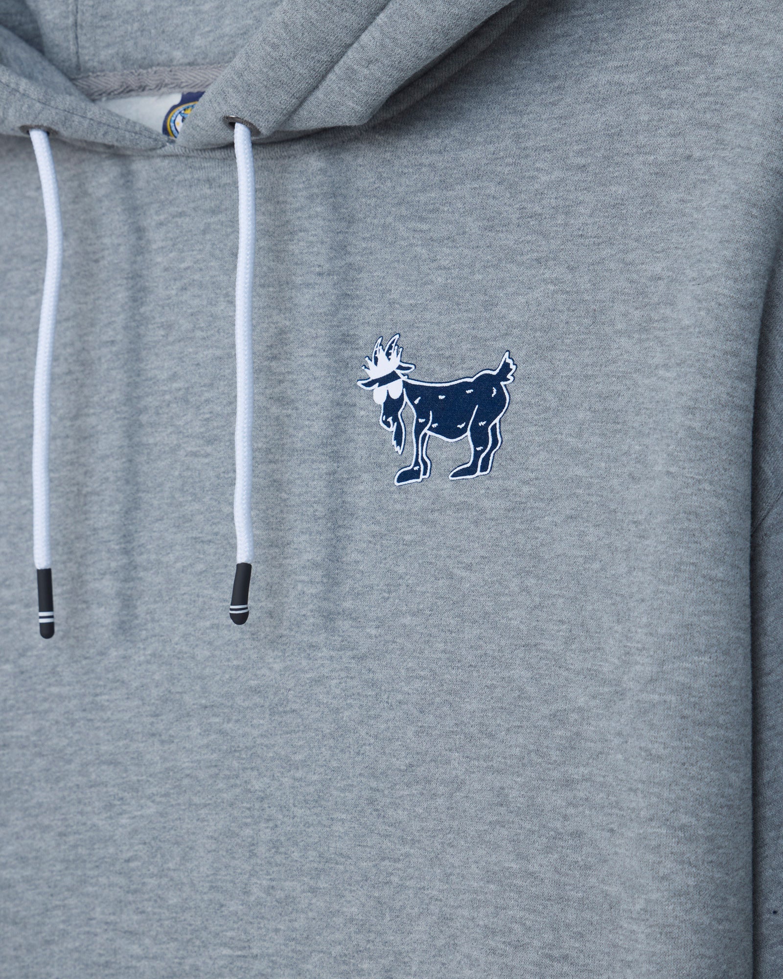 Close-up of a heather gray hoodie with white drawstrings and a small navy goat logo embroidered on the left chest.#color_gray