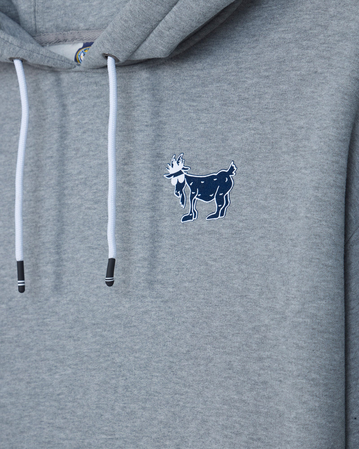 Close-up of a heather gray hoodie with white drawstrings and a small navy goat logo embroidered on the left chest.#color_gray