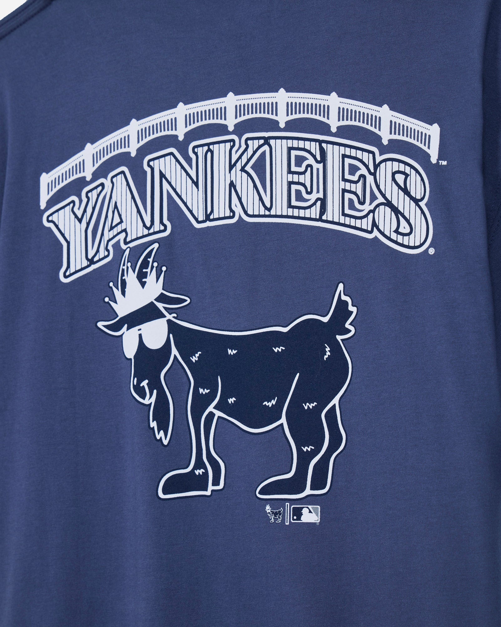 Close-up of a navy blue t-shirt featuring a white graphic of the New York Yankees logo, including the word 'YANKEES' in an arched font and a stylized goat mascot wearing sunglasses.#color_navy