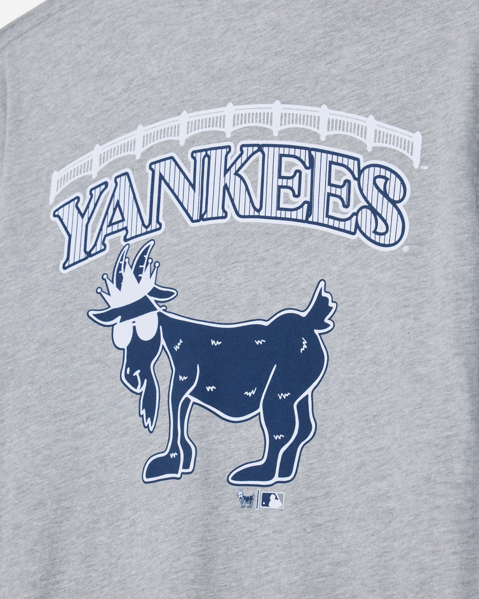 Close-up of a heather gray graphic T-shirt featuring the word 'YANKEES' in arched outlined letters above a navy blue goat logo, with a small MLB logo below.#color_gray