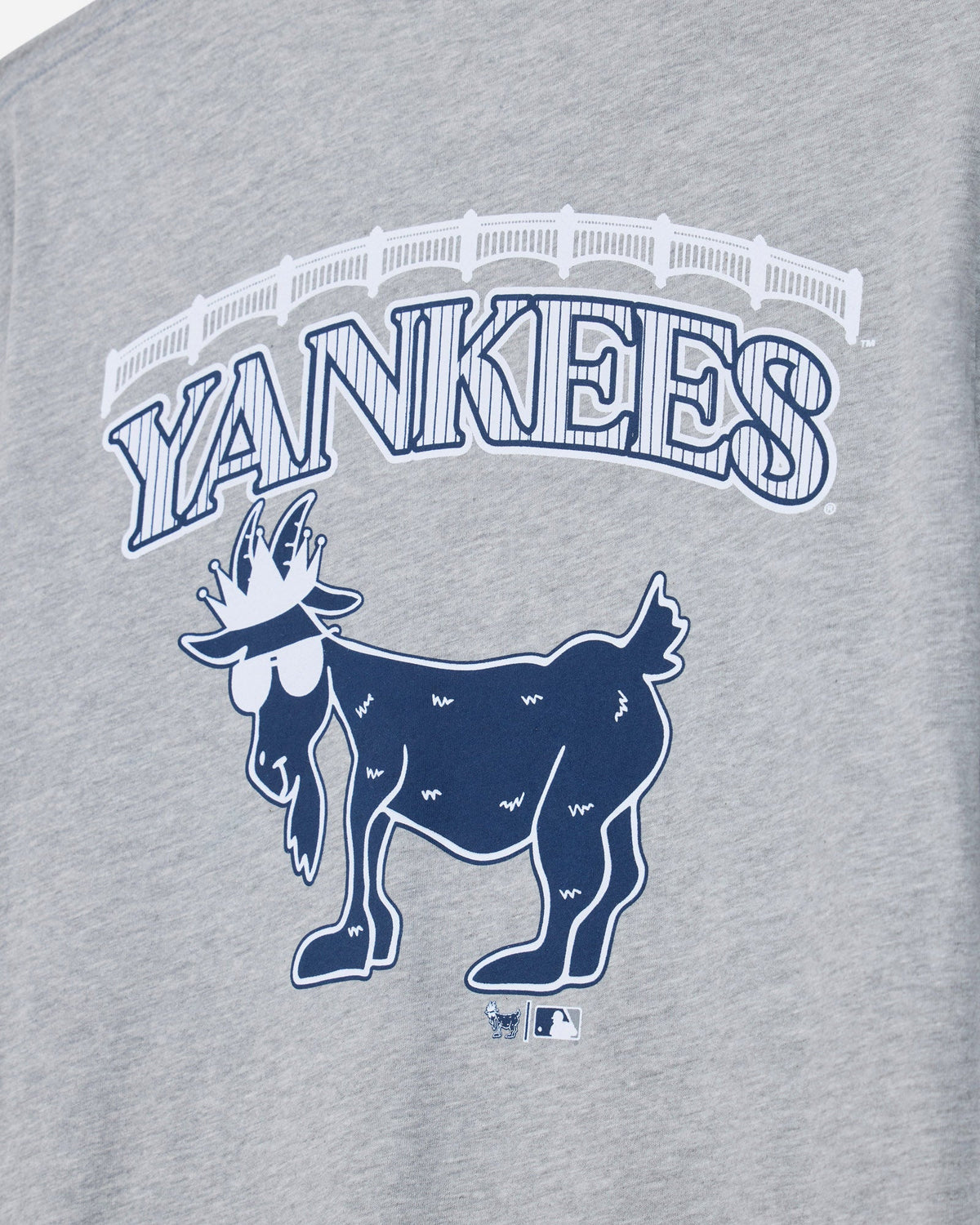 Close-up of a heather gray graphic T-shirt featuring the word 'YANKEES' in arched outlined letters above a navy blue goat logo, with a small MLB logo below.#color_gray
