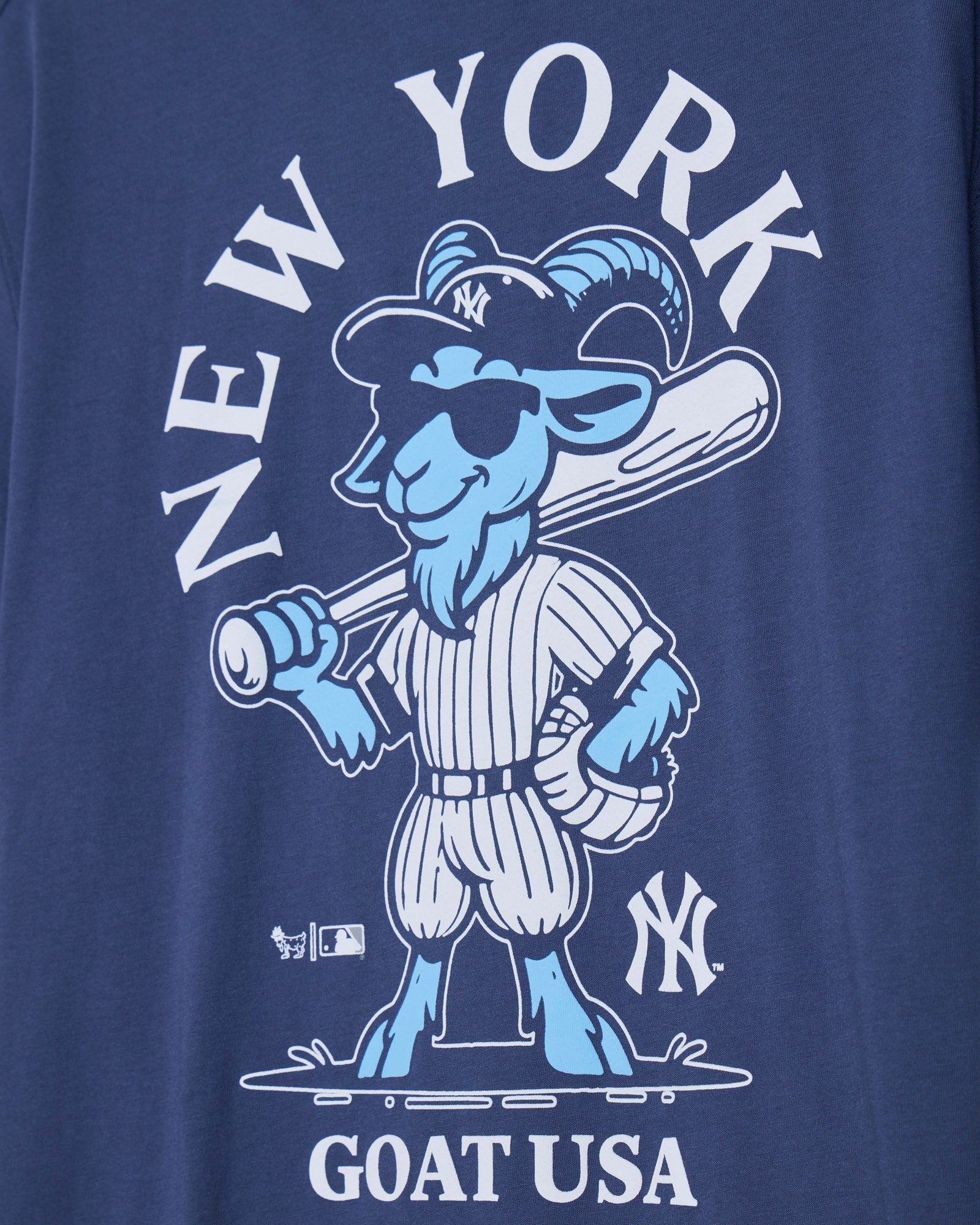 Close-up of a navy blue graphic t-shirt featuring a light blue and white cartoon goat baseball player with 'NEW YORK' above and 'GOAT USA' below.