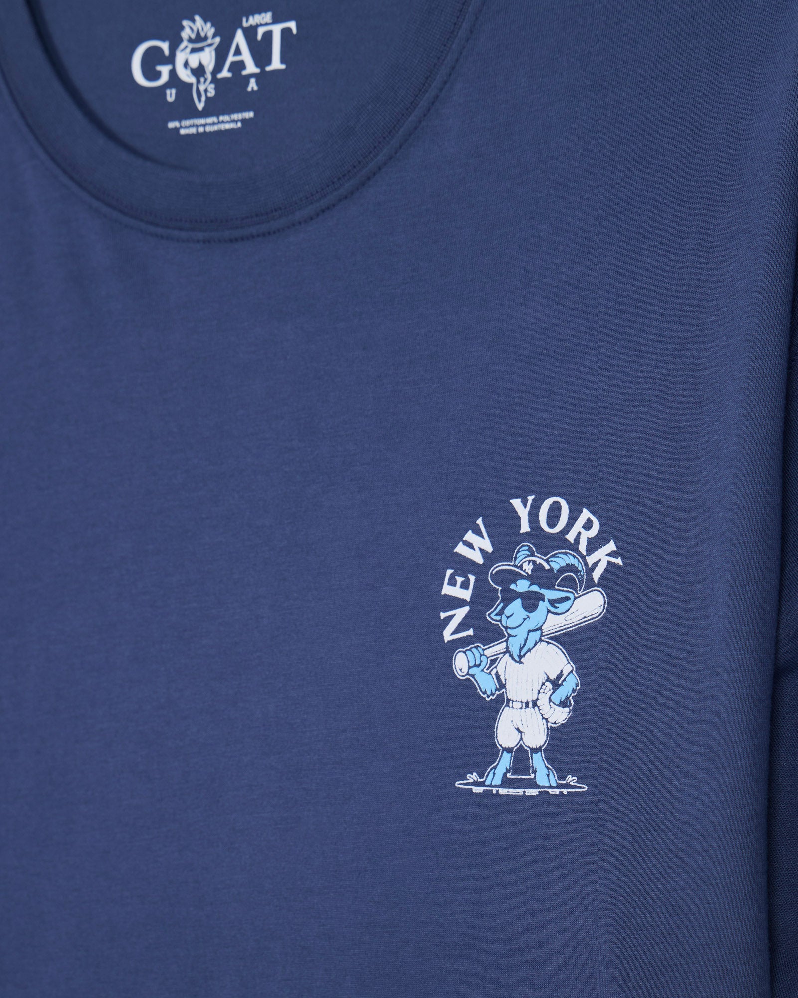 Close-up of a blue short-sleeve t-shirt featuring a light blue and white New York-themed cartoon graphic on the left chest with the text 'NEW YORK' arched above it.
