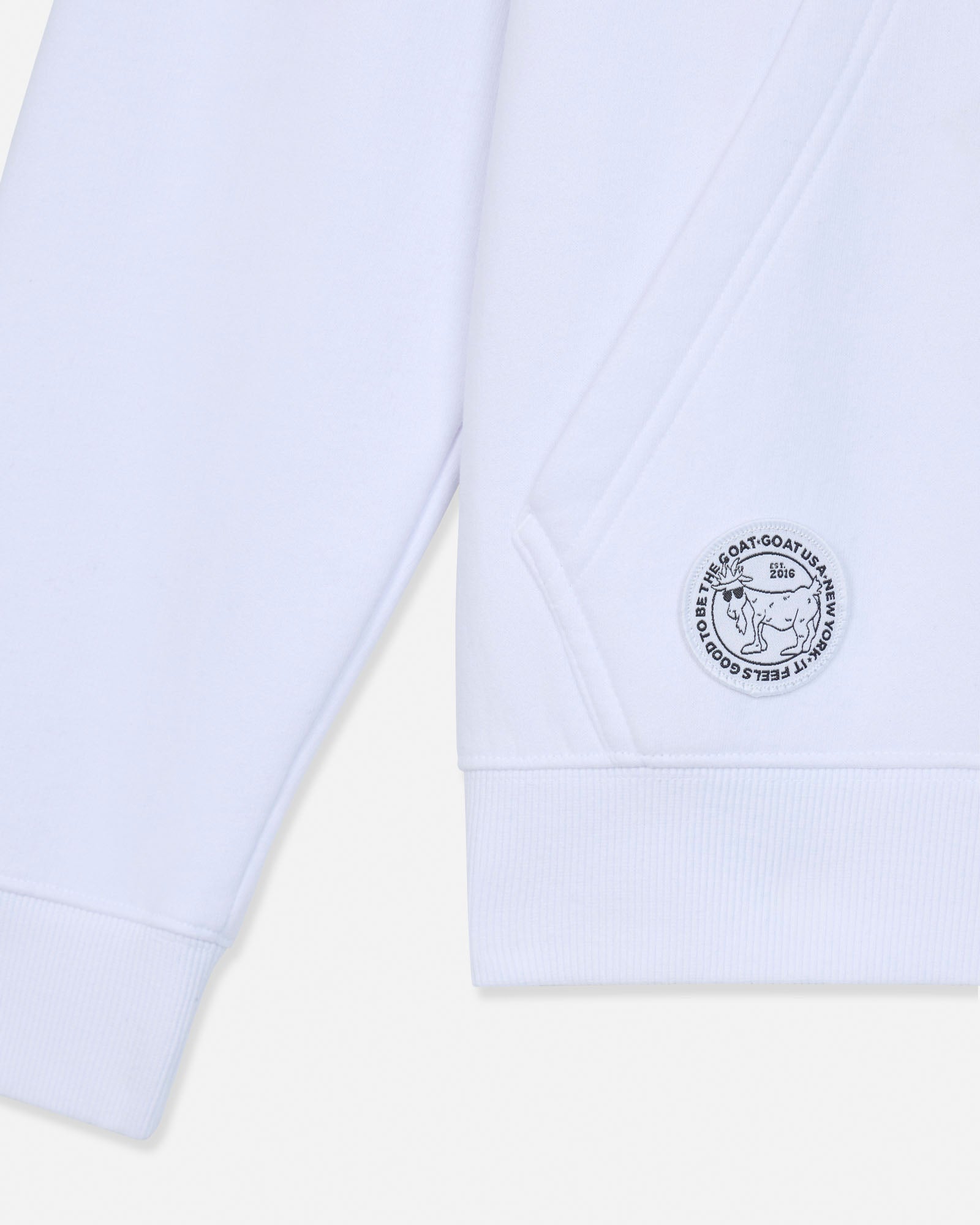 Close-up of a white sweatshirt sleeve with a circular embroidered logo patch on the cuff, photographed against a light neutral background.#color_white