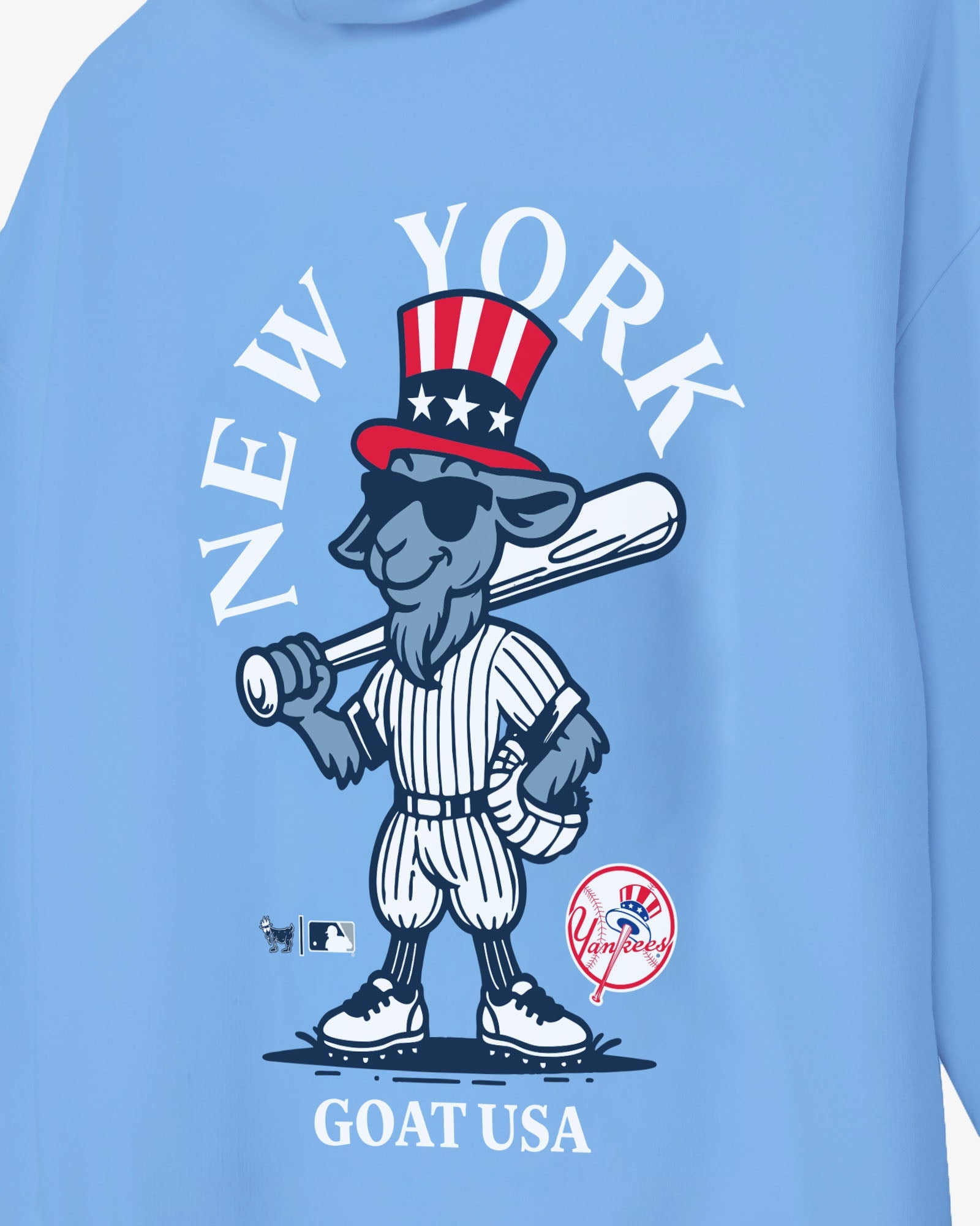 A close-up of a light blue sweatshirt featuring a cartoon goat baseball player wearing a red, white, and blue Uncle Sam hat, with the text 'NEW YORK' arched above and 'GOAT USA' below.#color_carolina-blue