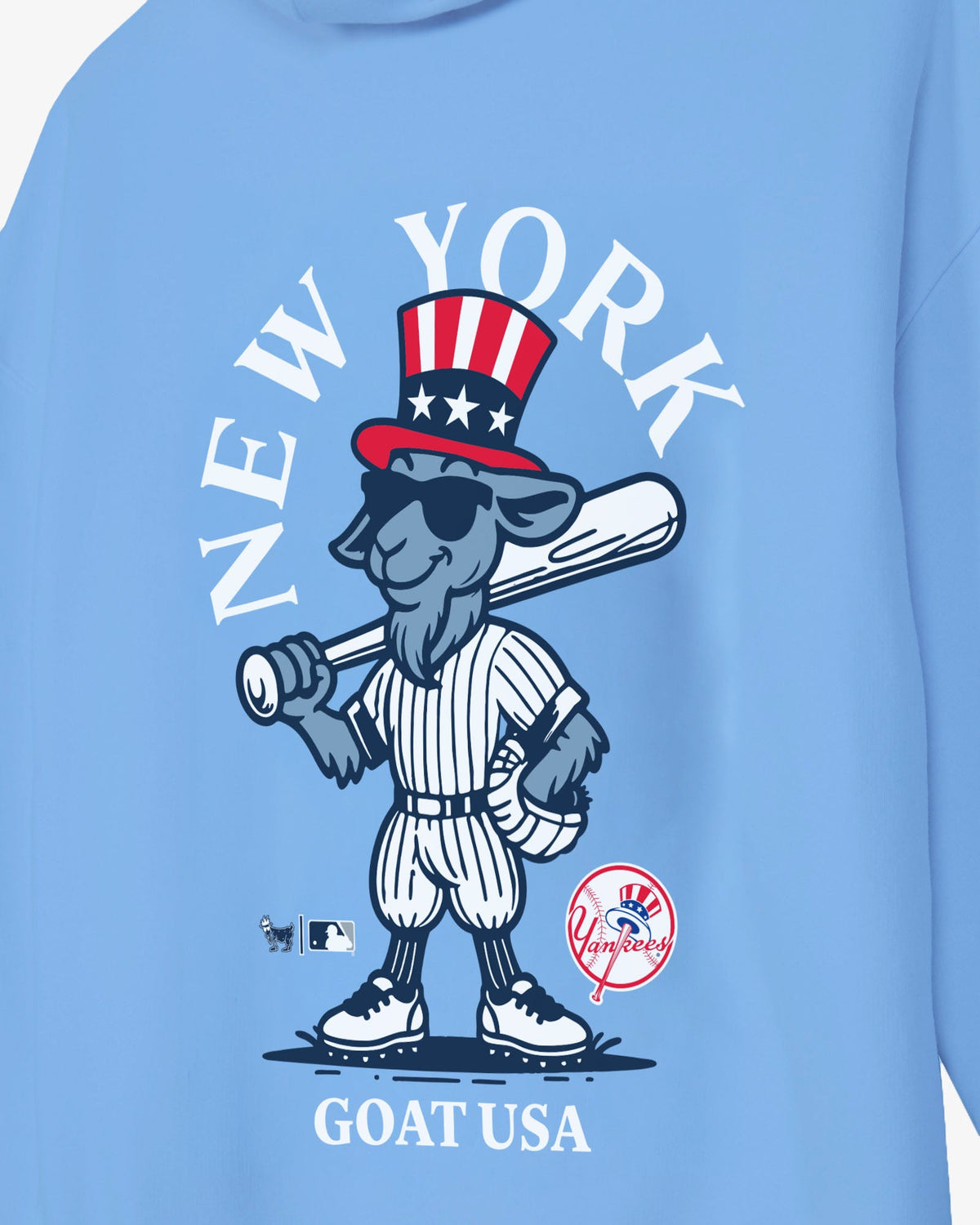 A close-up of a light blue sweatshirt featuring a cartoon goat baseball player wearing a red, white, and blue Uncle Sam hat, with the text 'NEW YORK' arched above and 'GOAT USA' below.