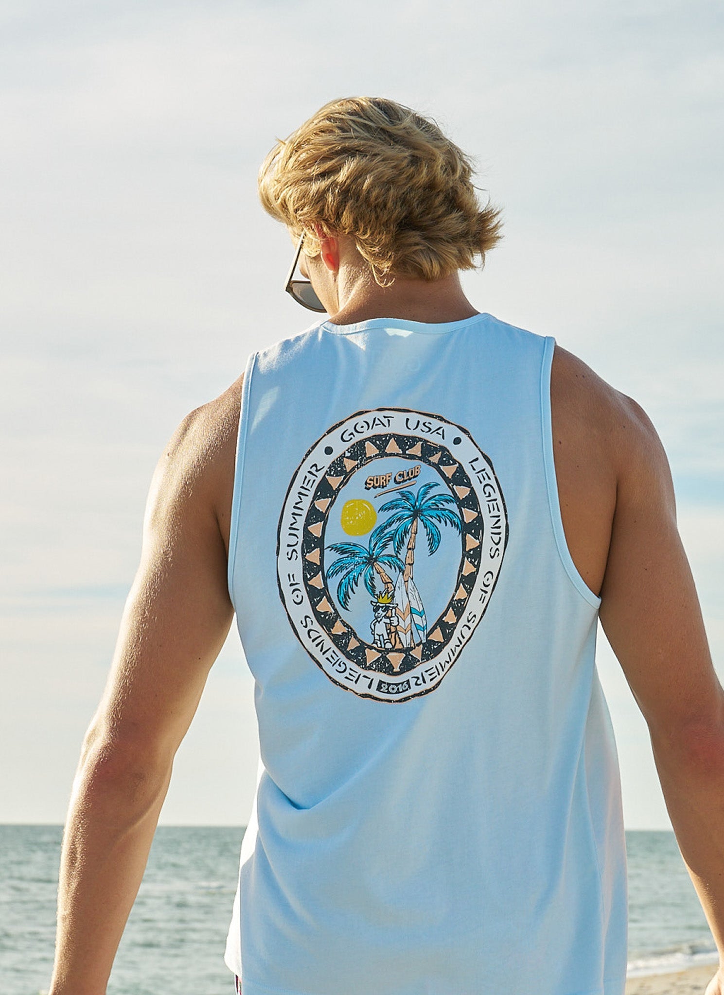 Guy wearing a blue tank top and sunglasses with the ocean in the background