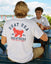 Man in white t-shirt with red lobster goat design eating at a picnic table