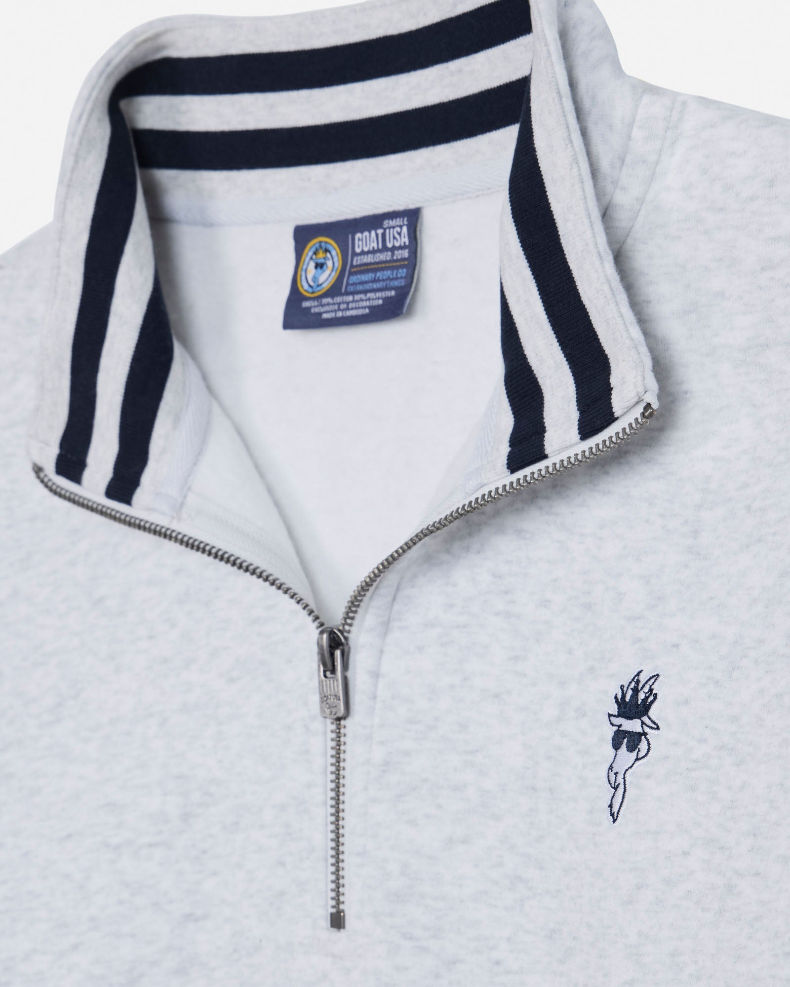 Close-up of a light heather gray quarter-zip pullover with a navy blue striped collar, a silver zipper, and a small navy embroidered logo on the left chest. A Coast USA label is visible inside the collar.#color_pale-gray