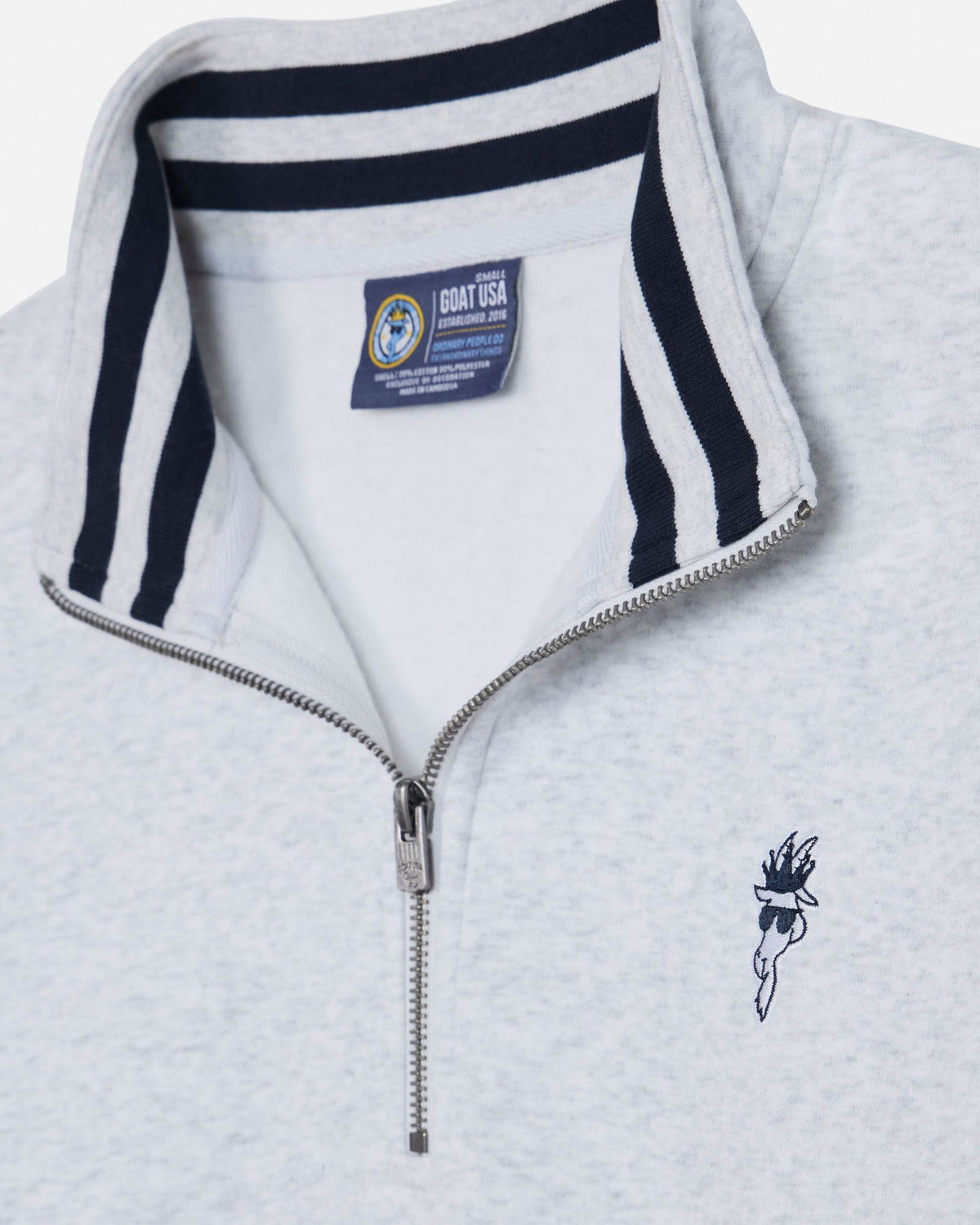 Close-up of a light heather gray quarter-zip pullover with a navy blue striped collar, a silver zipper, and a small navy embroidered logo on the left chest. A Coast USA label is visible inside the collar.