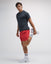 Man wearing a black t-shirt, red shorts, and white sneakers on a light gray background#color_poinsettia
