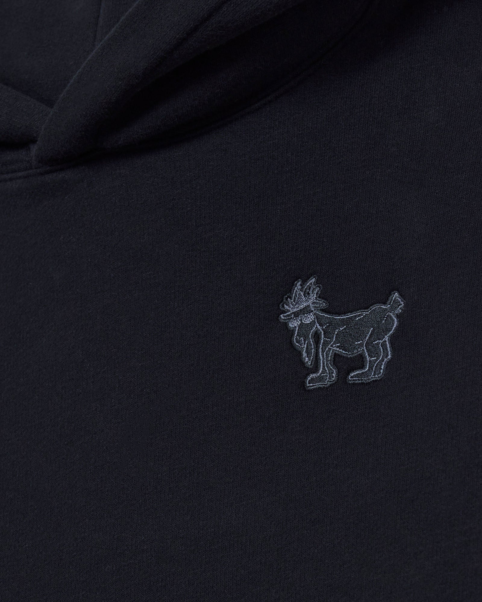Black fabric with a small embroidered logo of a goat on a dark background#color_black
