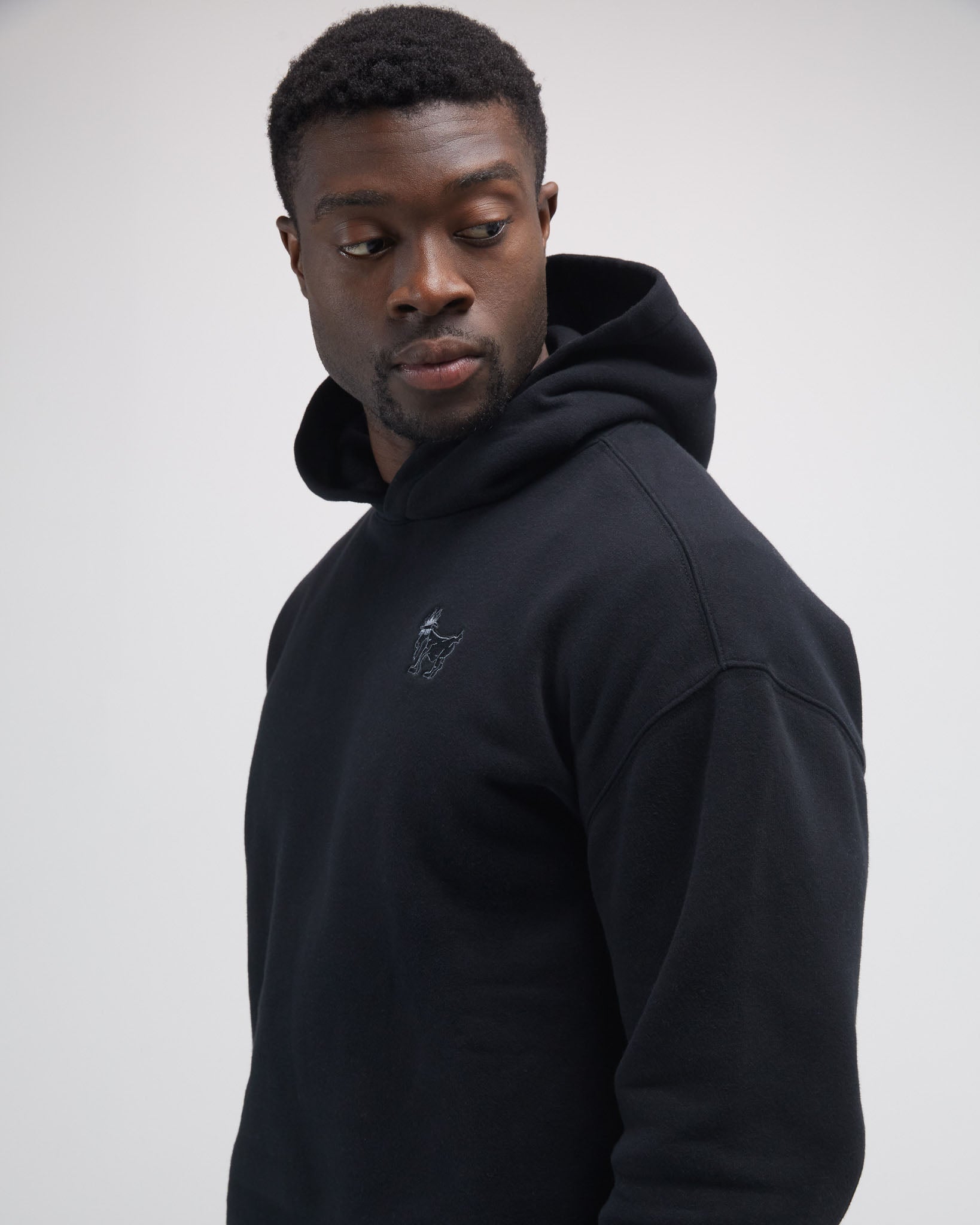 Man wearing a black hoodie with a logo on a light gray background#color_black