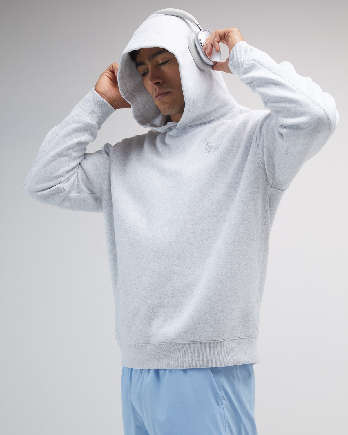 Person wearing a light gray hoodie and blue shorts on a plain background
