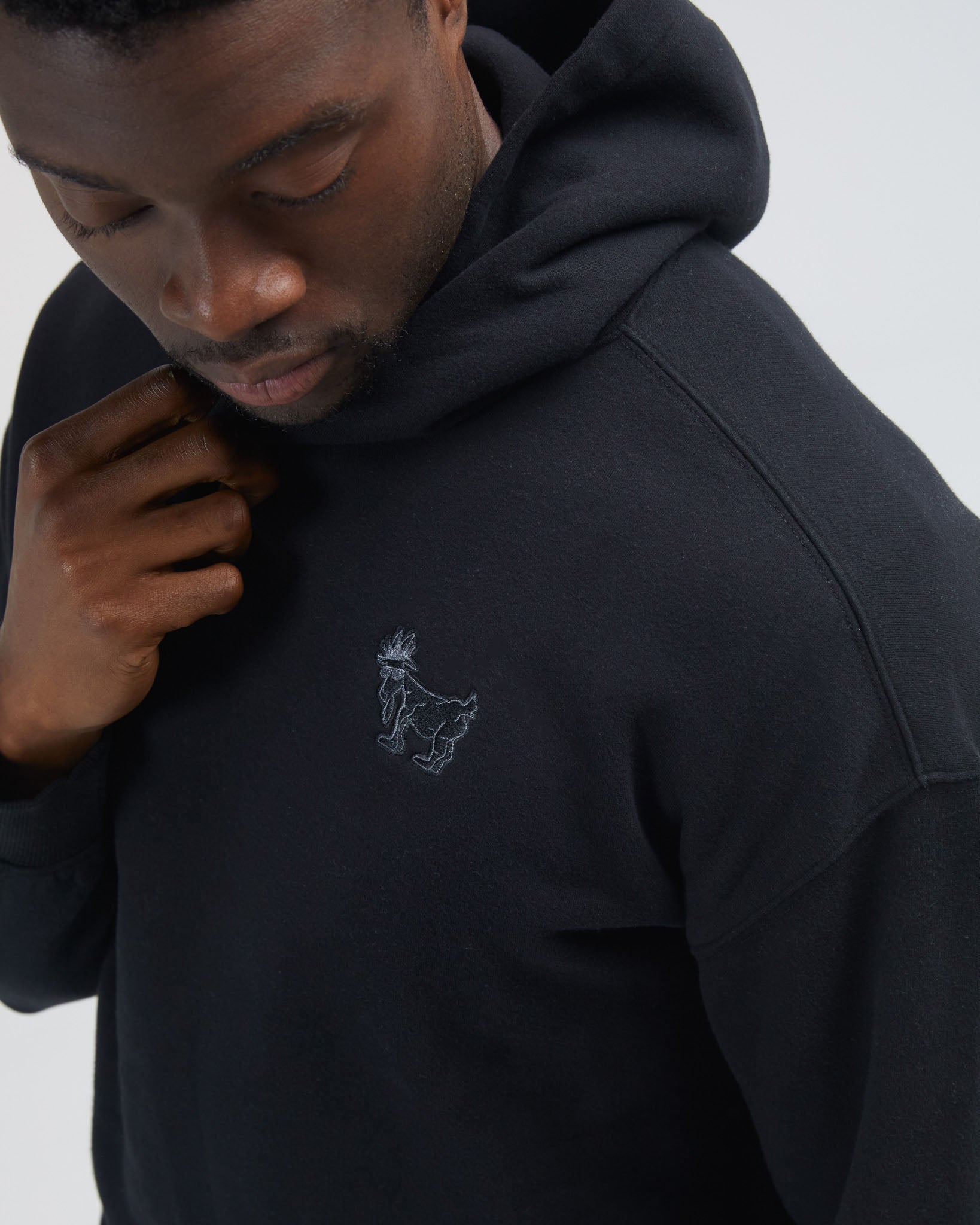Person wearing a black hoodie with a small logo on a light gray background#color_black