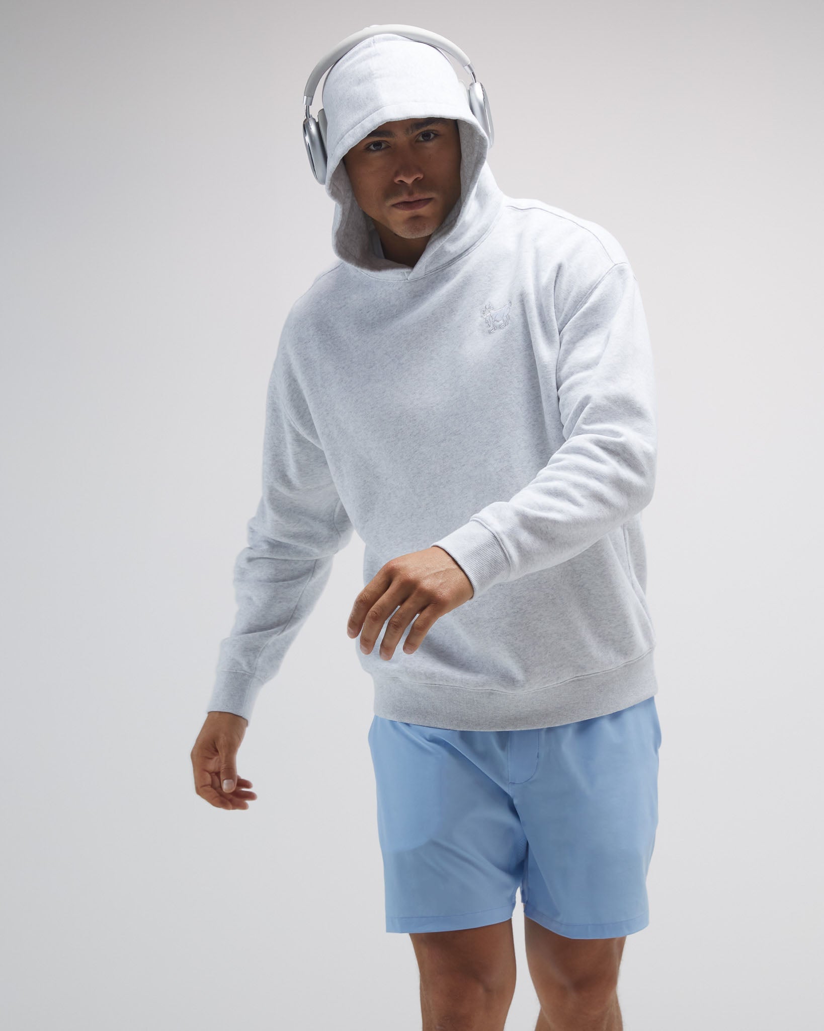 Person wearing a light gray hoodie and blue shorts on a plain background#color_pale-gray