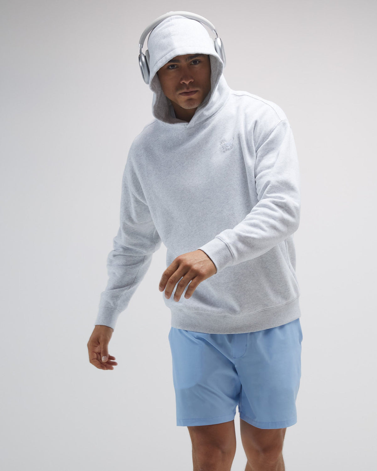 Person wearing a light gray hoodie and blue shorts on a plain background