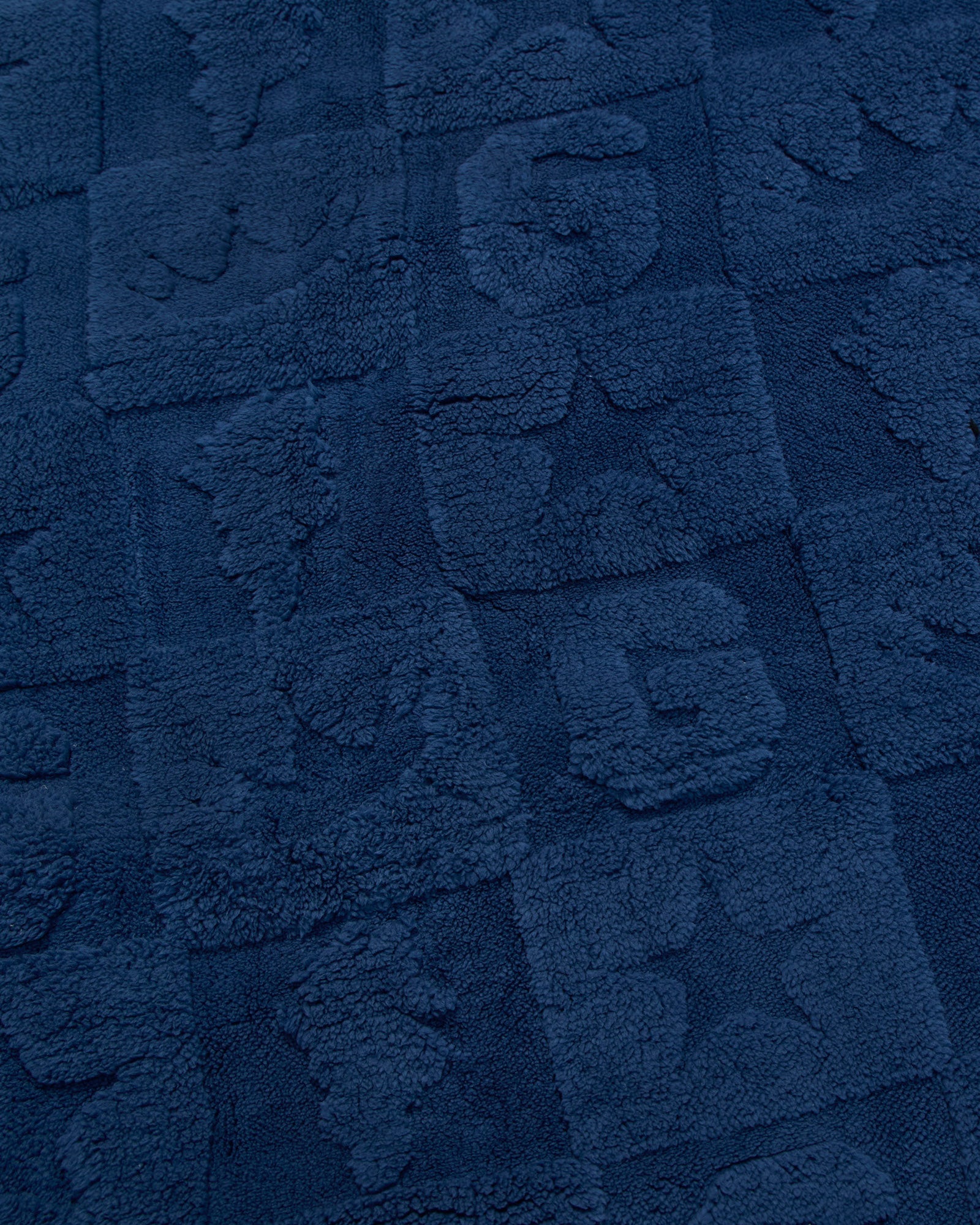 A close-up of a dark navy blue textured fabric with raised block patterns and tufted lettering.