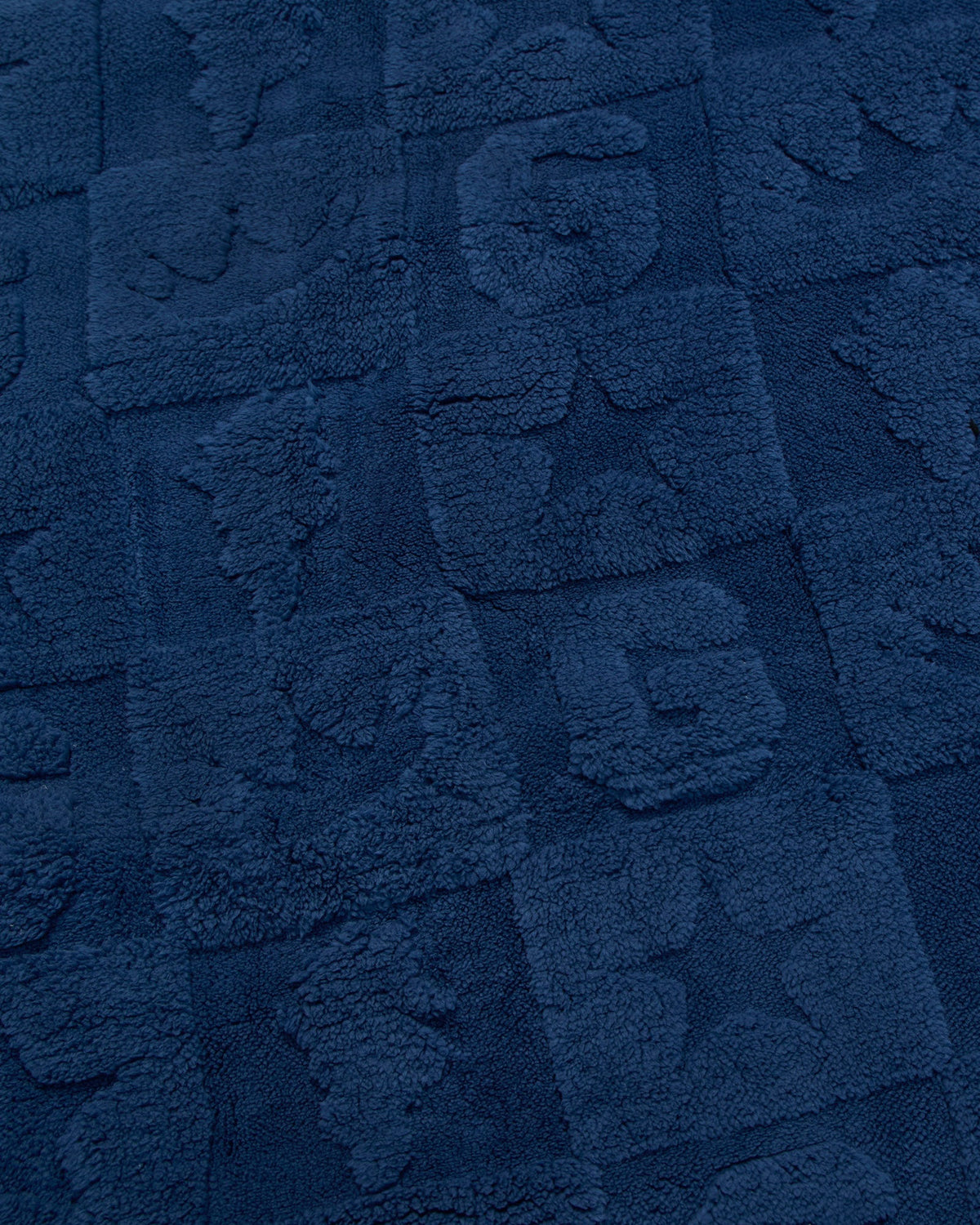 A close-up of a dark navy blue textured fabric with raised block patterns and tufted lettering.
