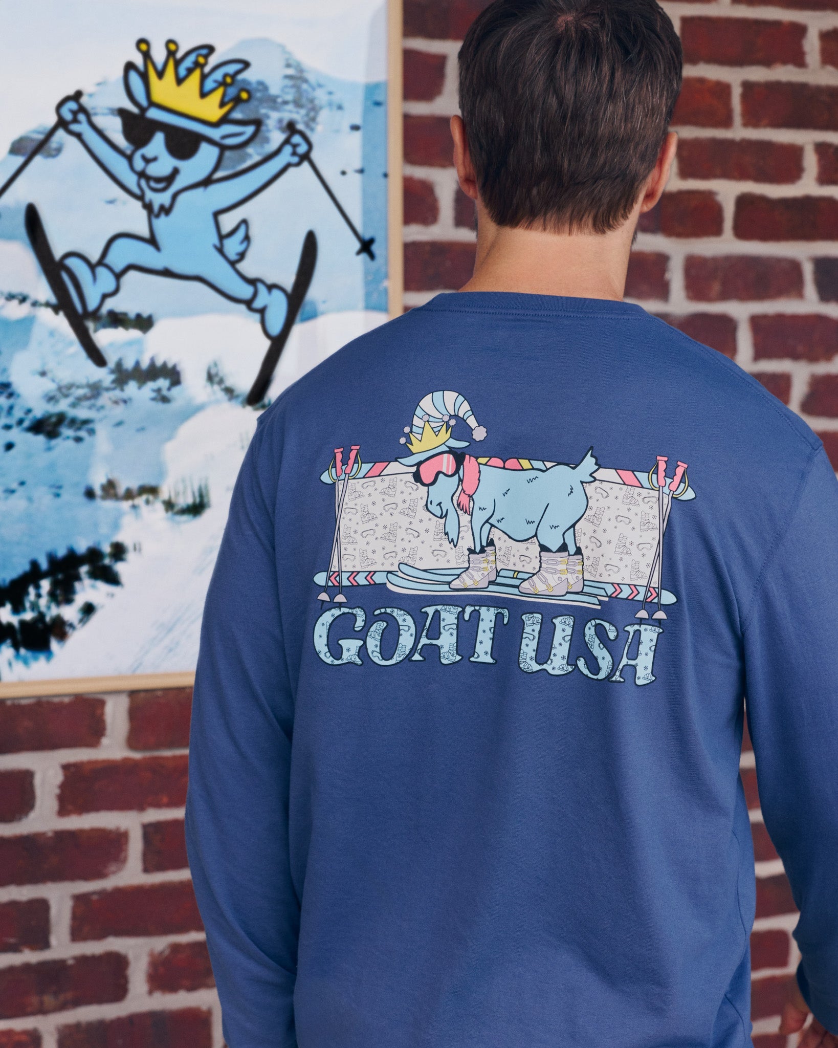 Person wearing a blue long-sleeve shirt with 'GOAT USA' graphic, standing in front of a brick wall.
