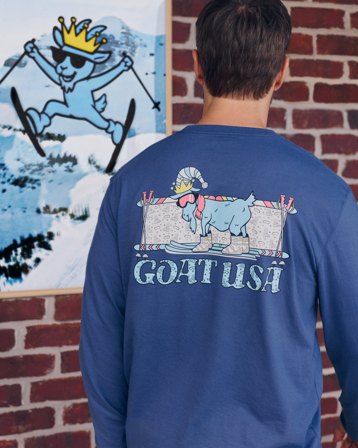 Person wearing a blue long-sleeve shirt with 'GOAT USA' graphic, standing in front of a brick wall.