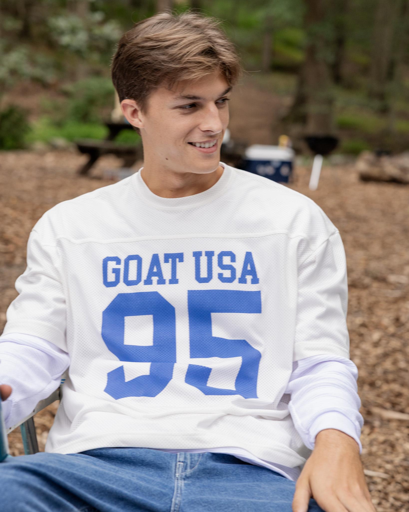Person wearing a white sweatshirt with 'GOAT USA 95' text, sitting outdoors.