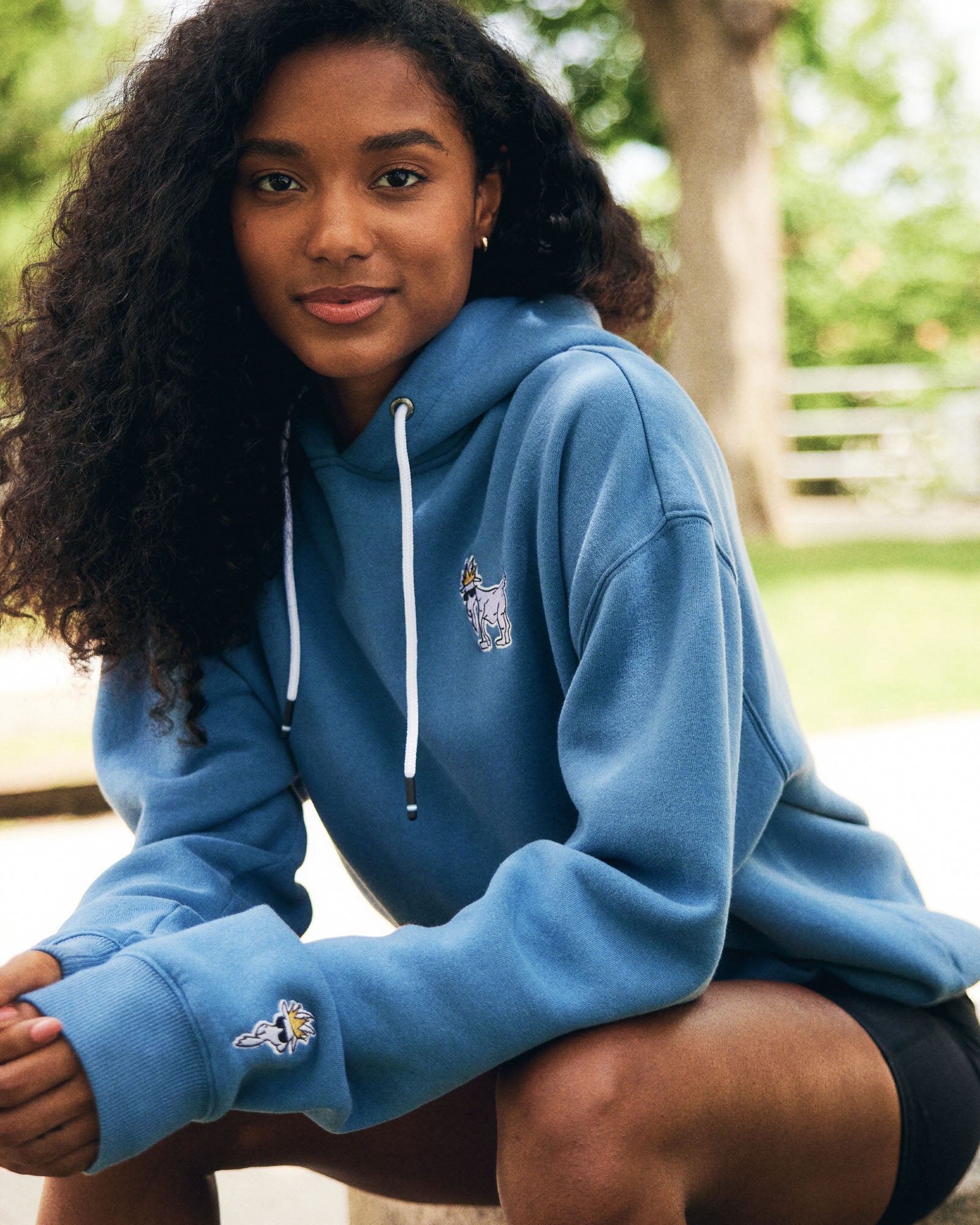 Person wearing a blue hoodie with a logo, sitting outdoors#color_coronet-blue