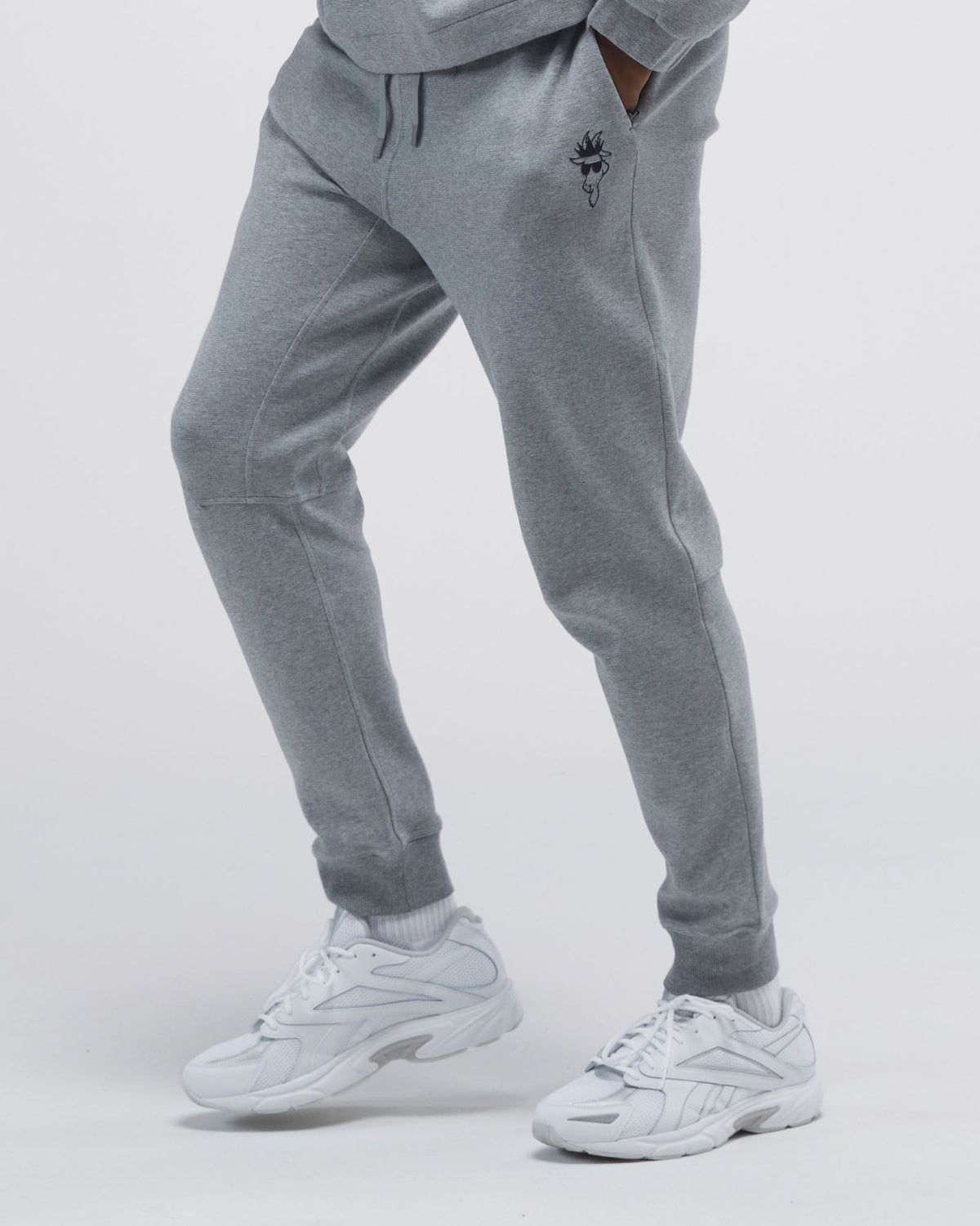 Person wearing gray jogger pants with a logo on a light gray background