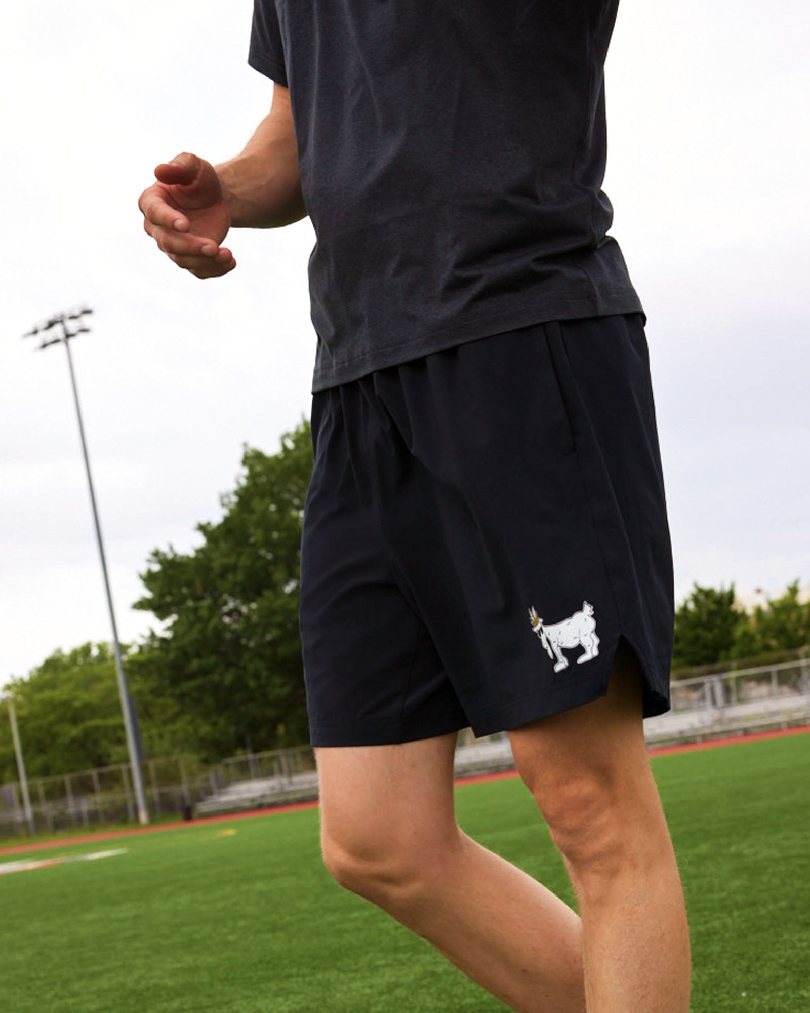 Person wearing black shorts with a small white logo on a sports field#color_black