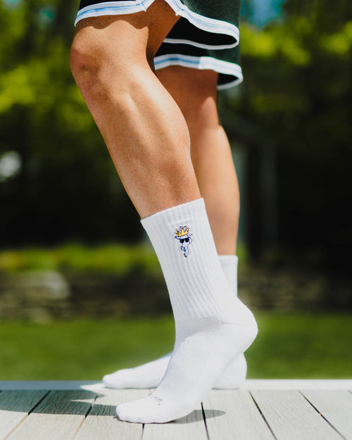 White socks with a logo worn by a person on a wooden deck with greenery in the background