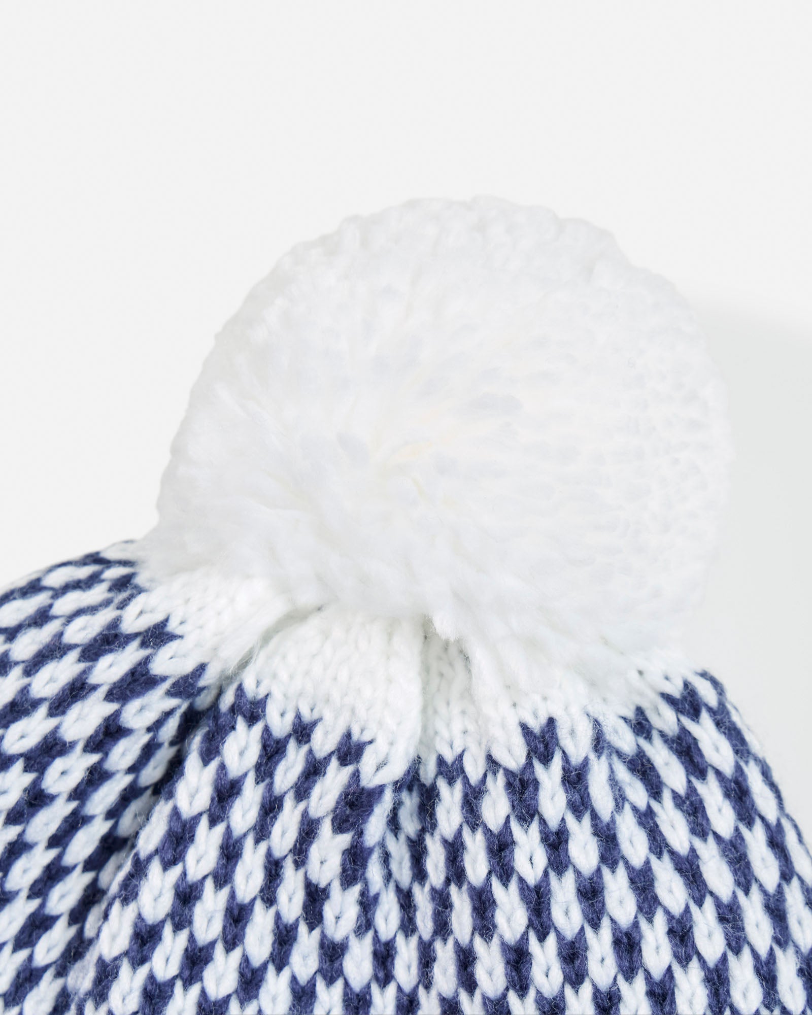 Close-up of a white and blue checkered fabric with a white pom-pom on a white background