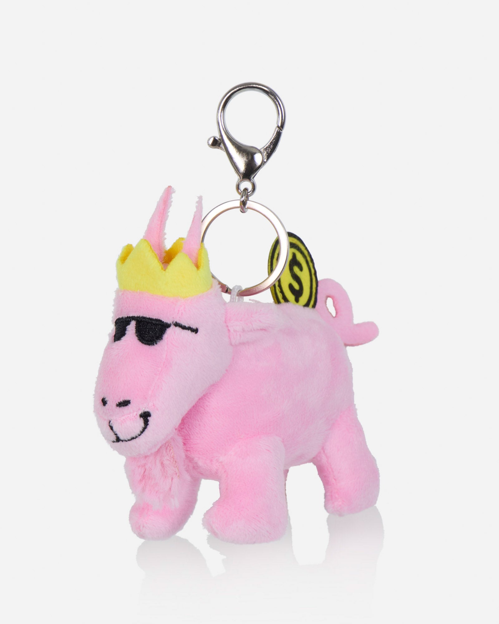 A pink plush bag charm shaped like a stylized animal character with a yellow crown, black sunglasses, and a metal clasp on a light gray background.