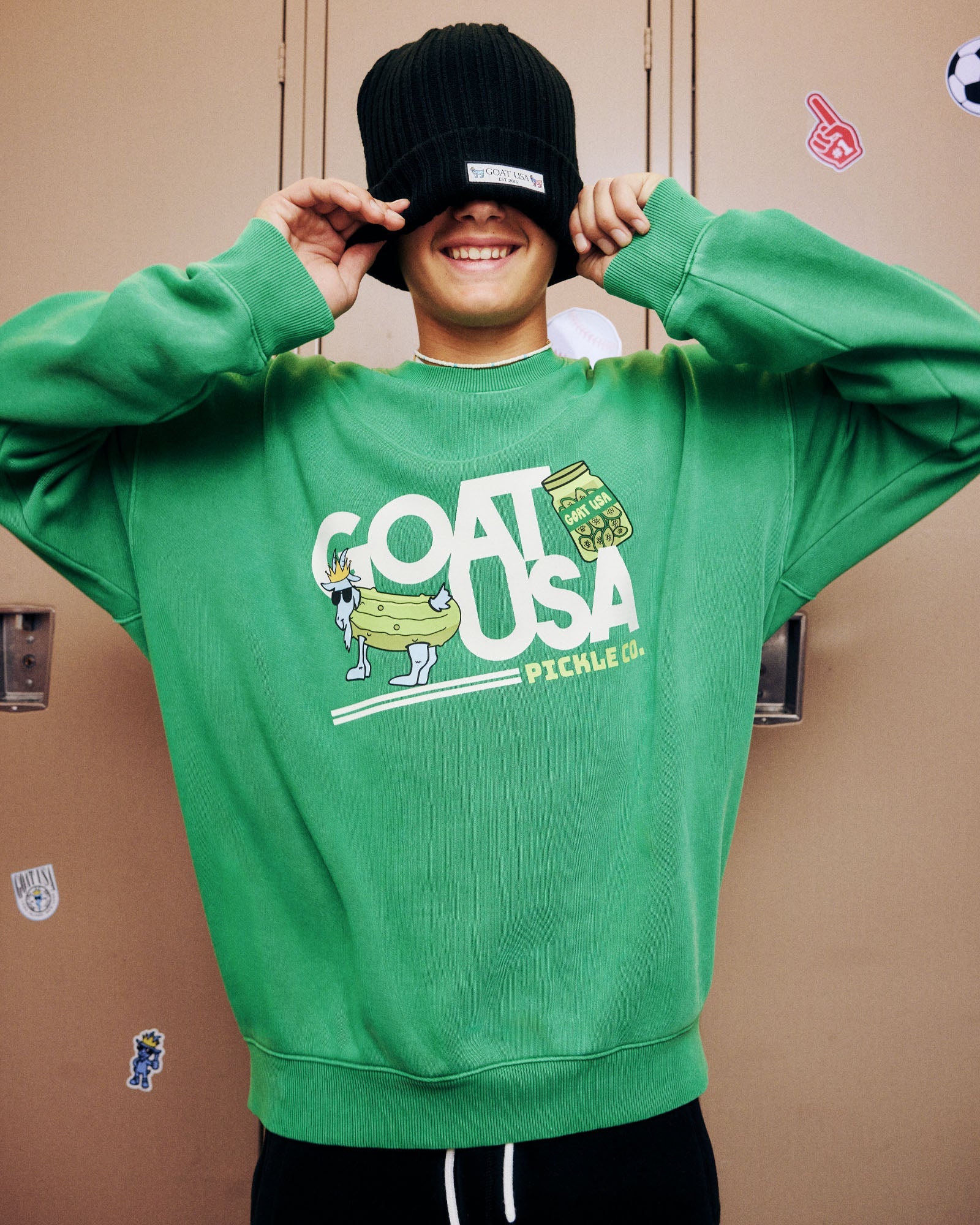 Person wearing a green sweatshirt with a graphic design in front of lockers.