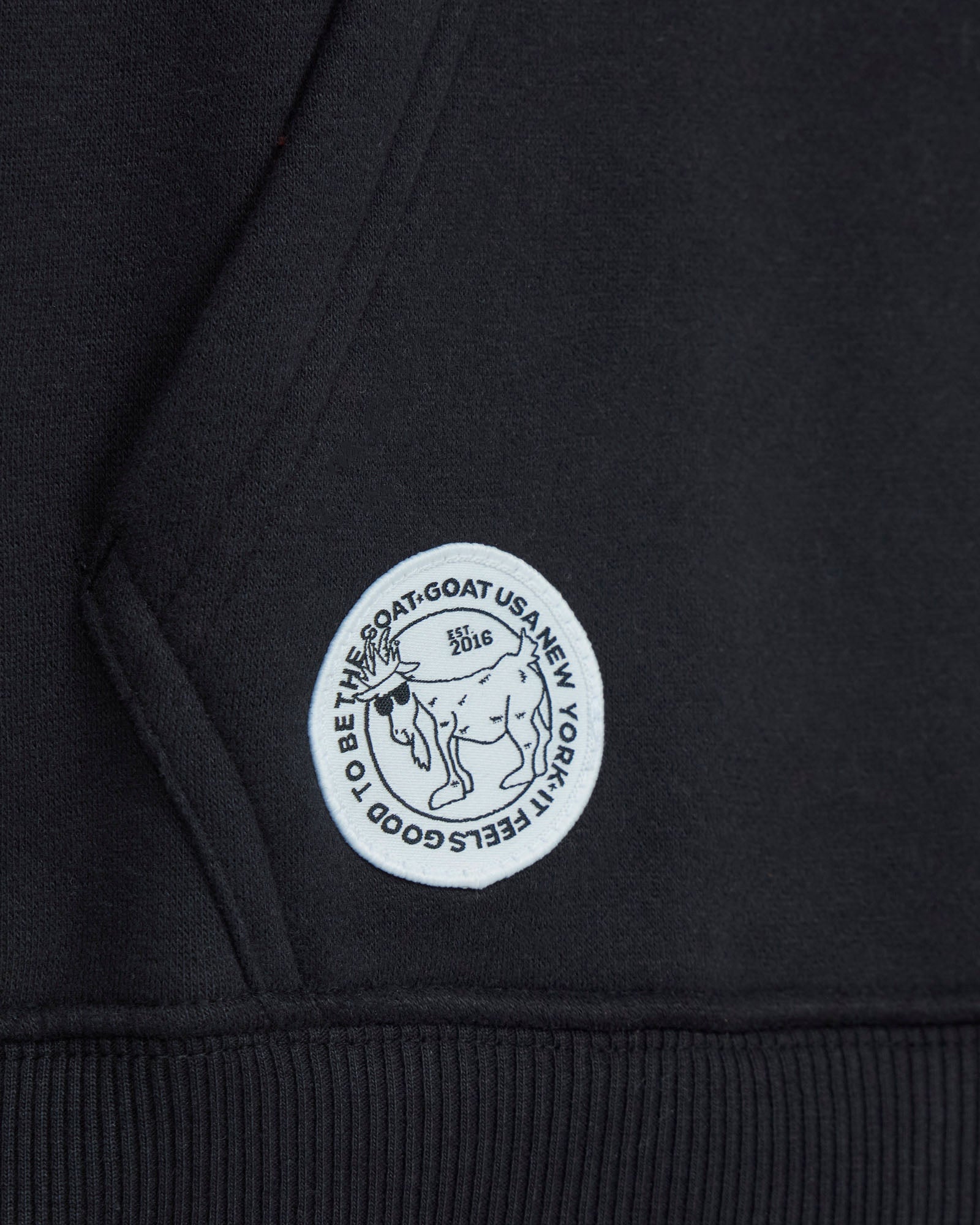 Close-up of a black hoodie with a white logo on a dark background#color_black