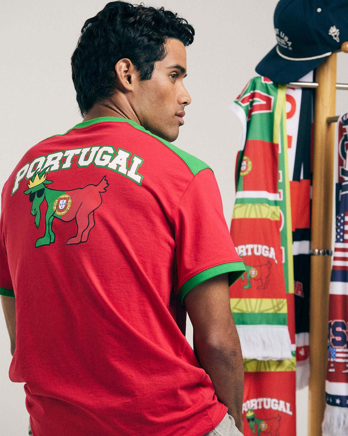 Man wearing a red Portugal t-shirt with a goat emblem, standing in front of a rack with various flags.