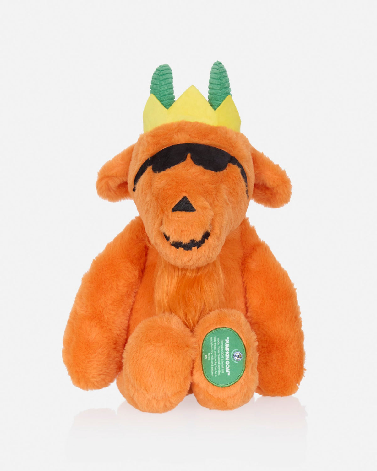 An orange plush goat toy with green horns wearing a yellow crown and black sunglasses, photographed against a clean white background.