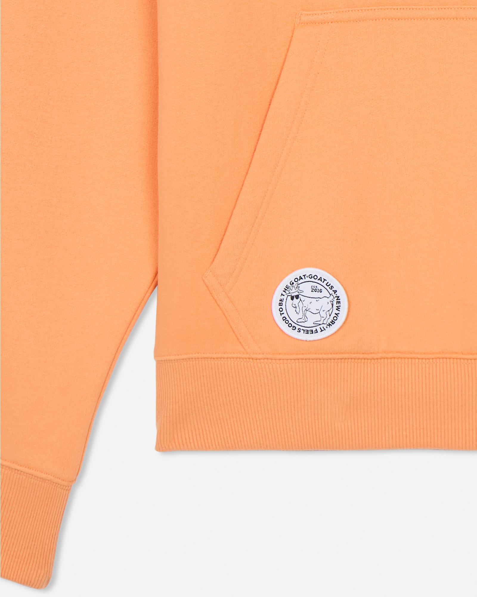 Close-up of an orange sweatshirt with a logo on a light gray background