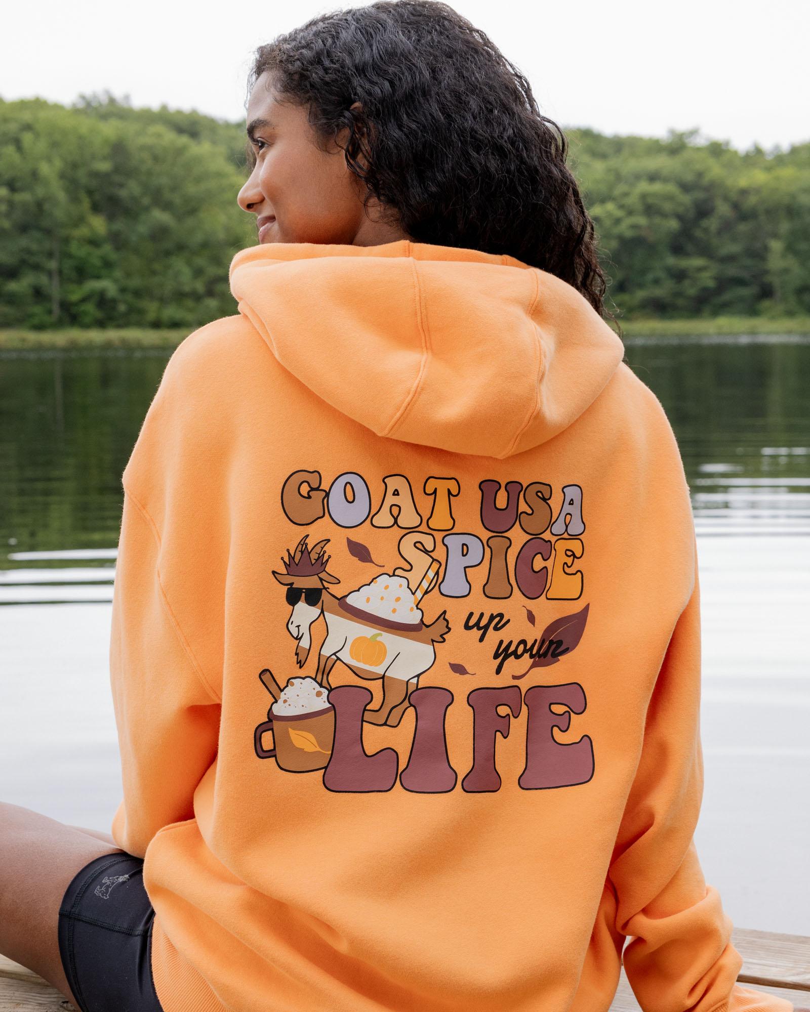 Person wearing an orange hoodie with a graphic and text by a lake
