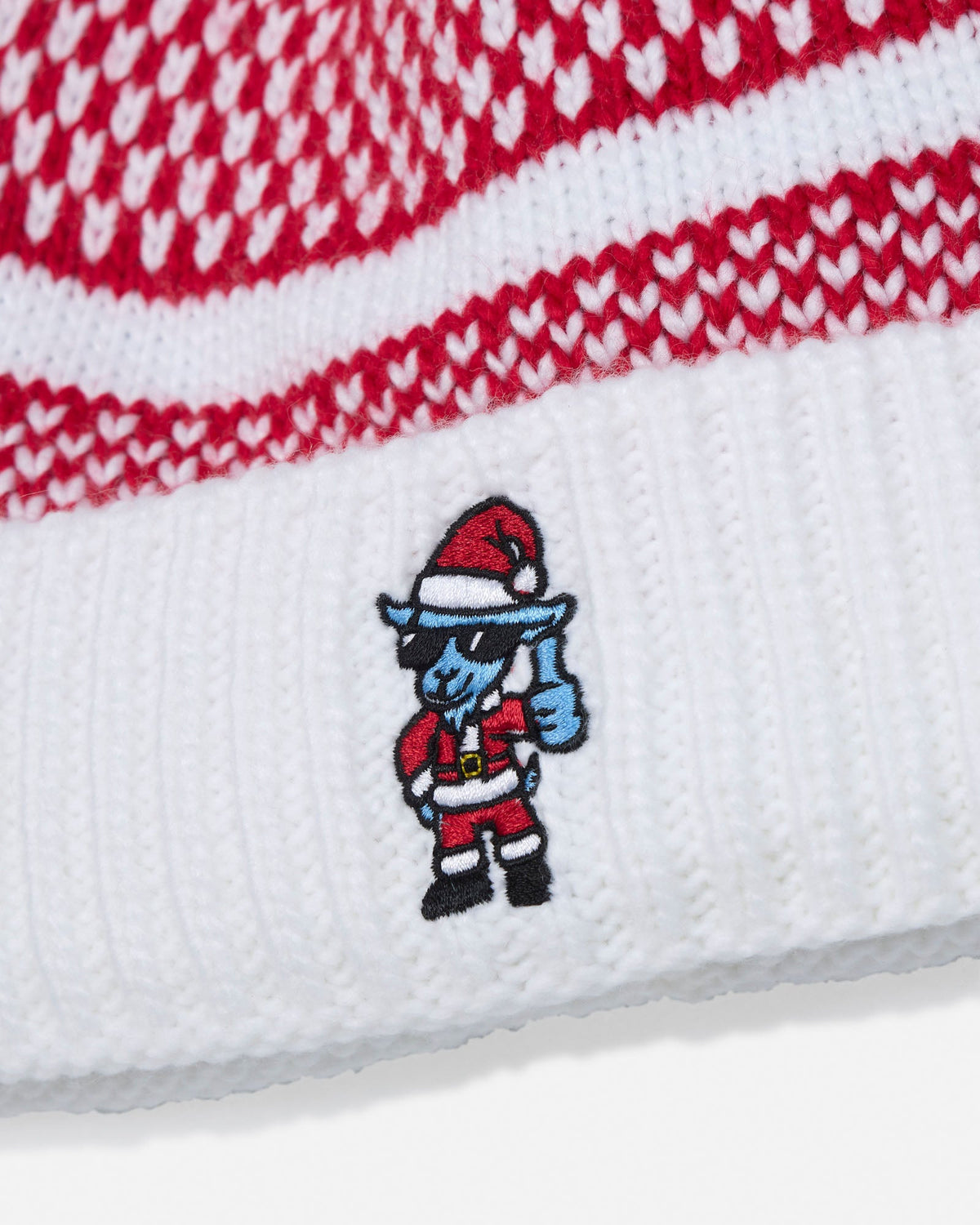 Close-up of a white knit beanie with red heart-patterned stripes and an embroidered Santa-clad blue character on the cuff.