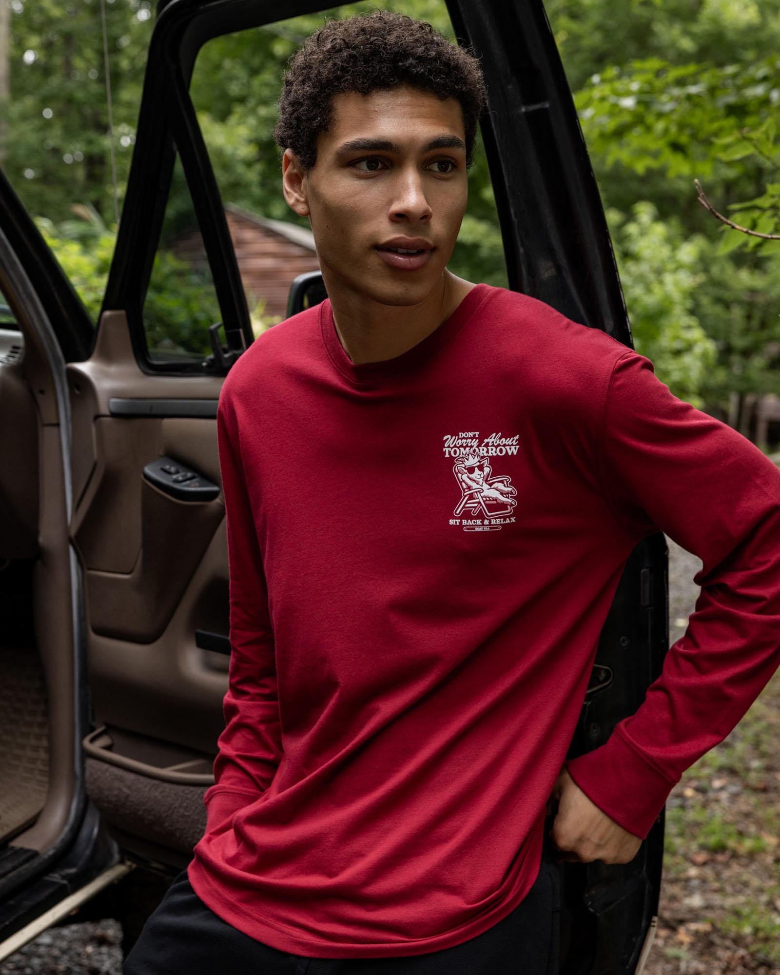 Person wearing a red long-sleeve shirt with a logo, standing next to an open car door outdoors.