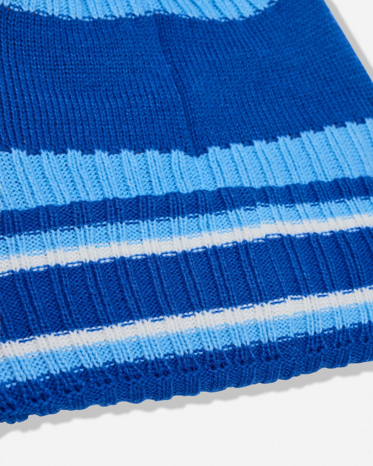 A close-up of a ribbed knit beanie with horizontal stripes in royal blue, medium blue, light blue, and white.